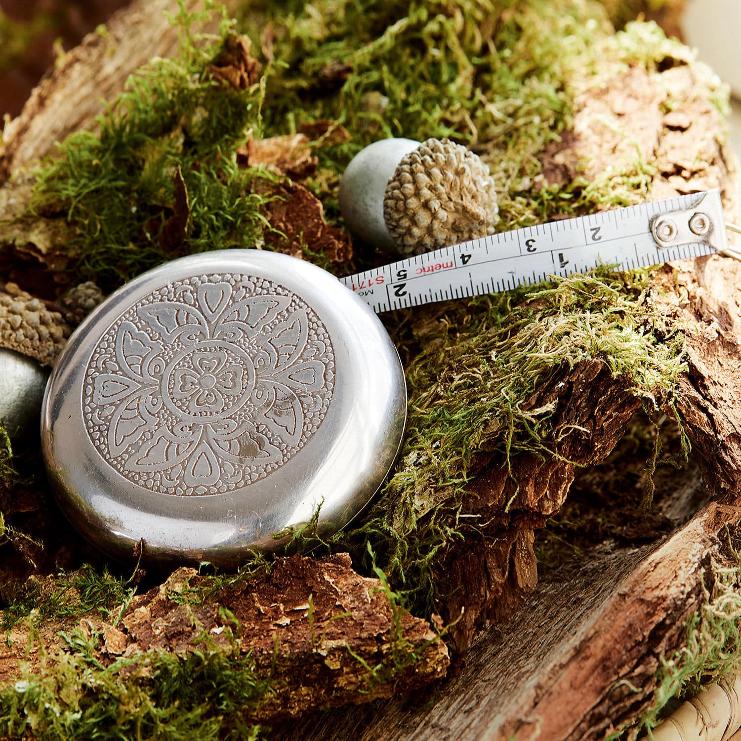Meetlint Jesolo Metalen meetlint met bloemmotief op mosbedekt hout, praktisch meetinstrument