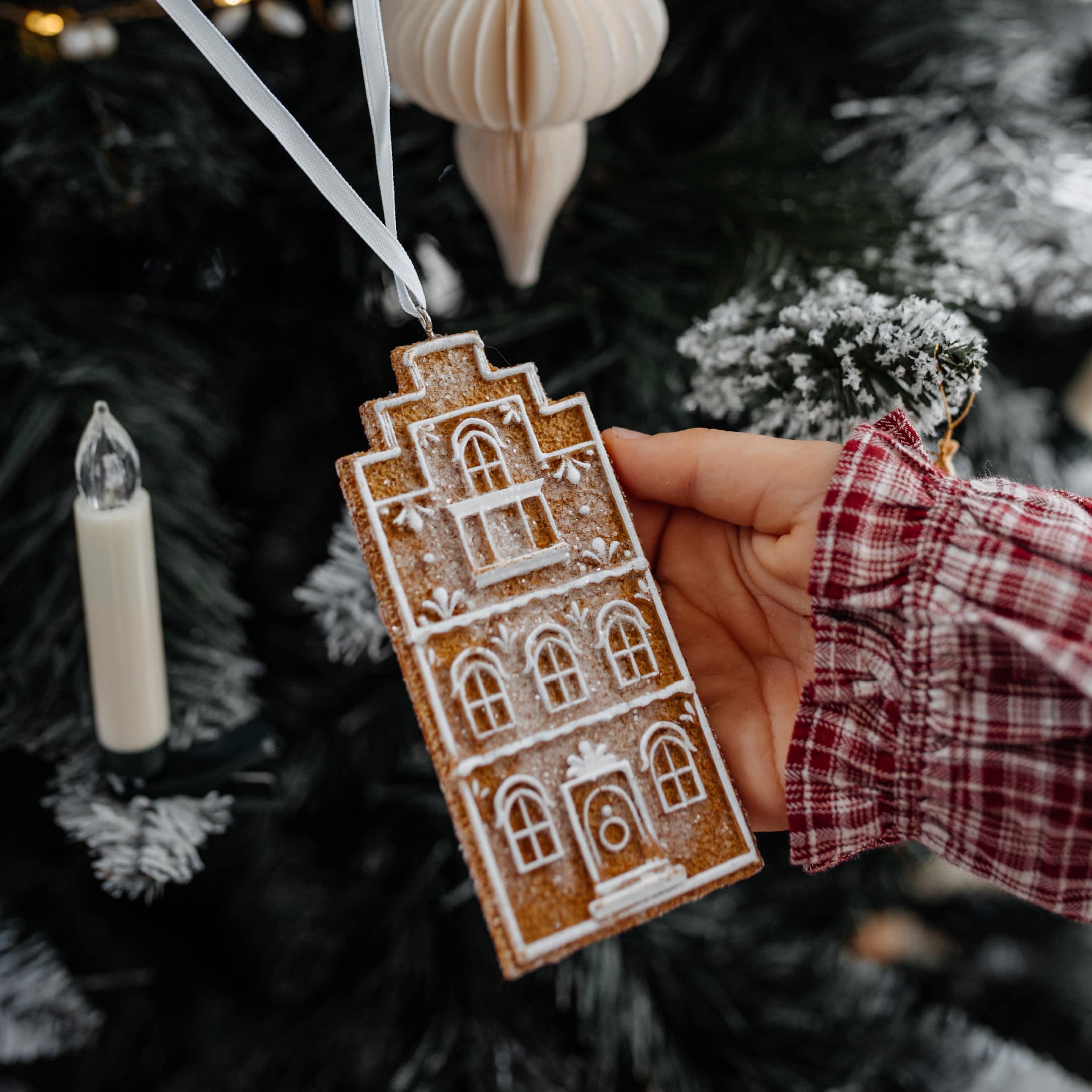 Kerstversiering in de vorm van een peperkoekhuisje met wit patroon, hangend aan een wit lint