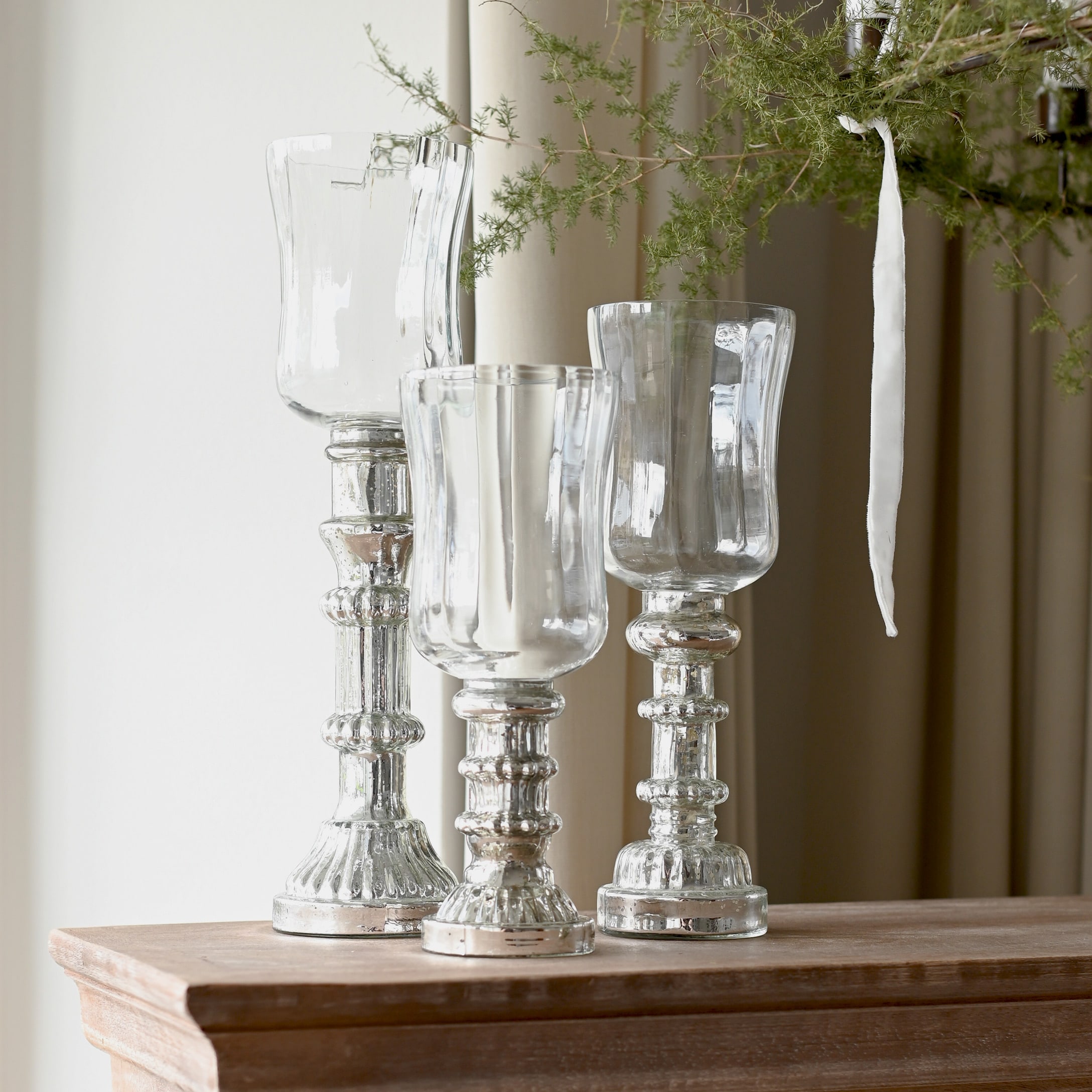 Drie decoratieve kandelaars van glas en zilverkleurig metaal op een houten blad