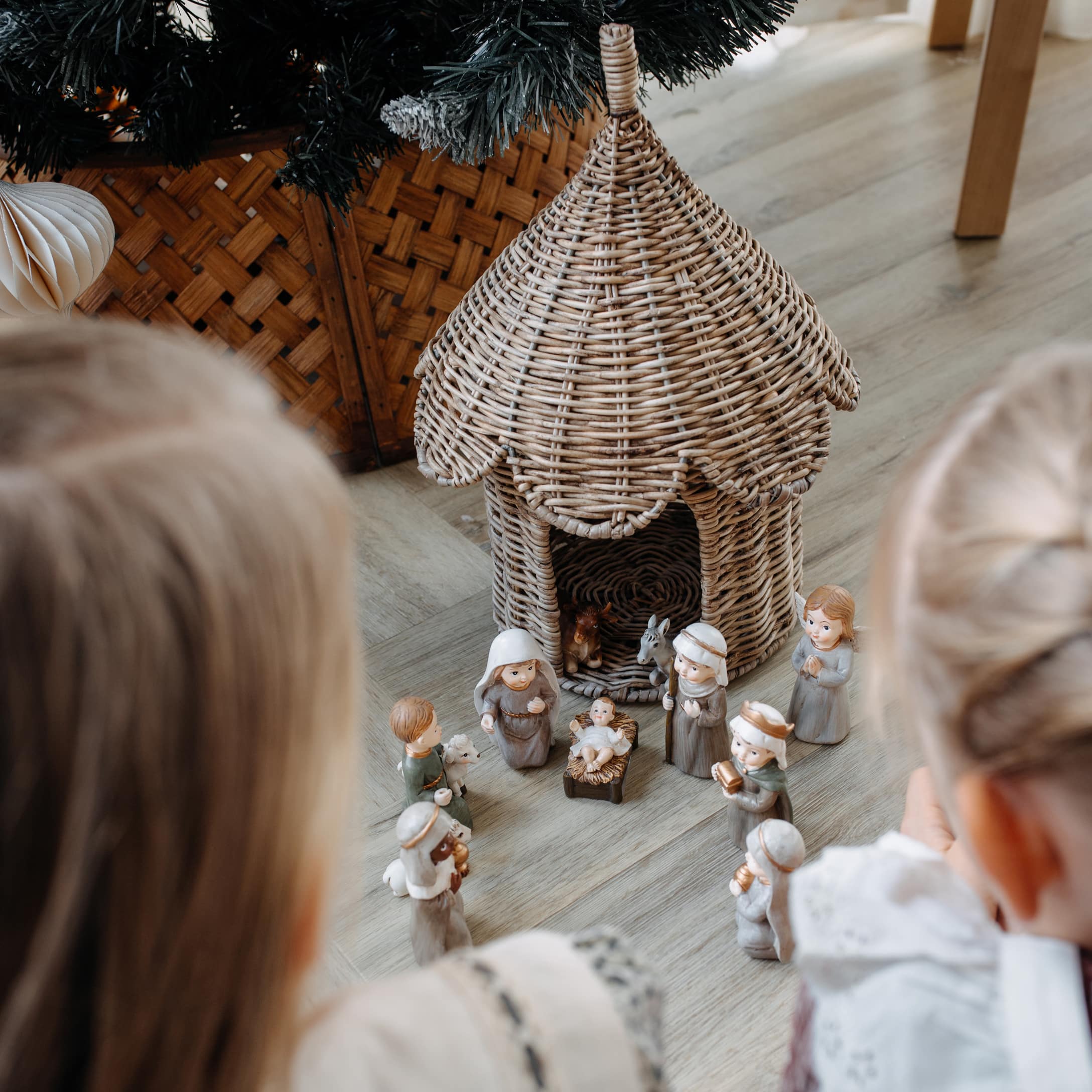 Kinderen kijken naar kerststal met keramische figuren en een rieten huisje op de vloer