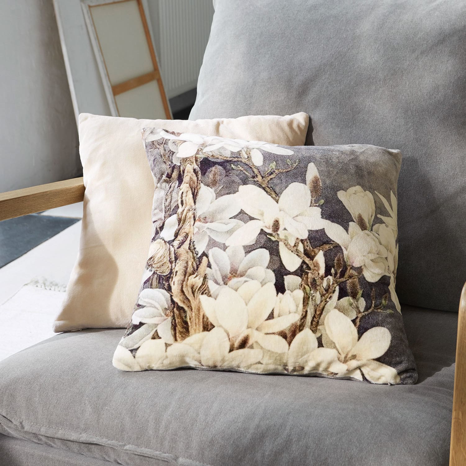 Decoratief kussen van zacht materiaal met bloemenpatroon in beige en grijstinten op een bank