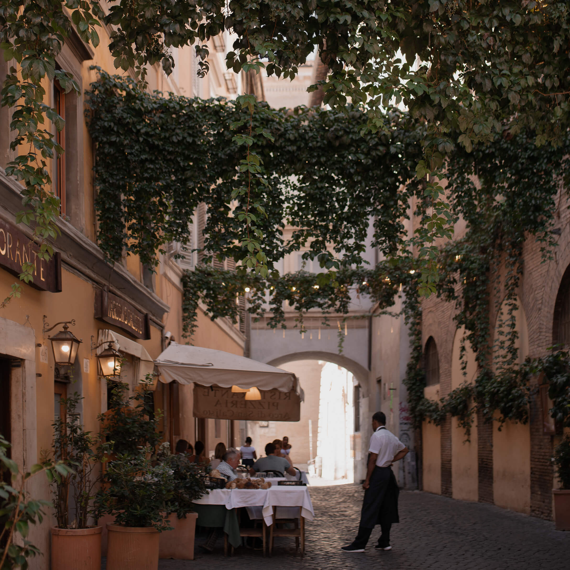 Kasseienstraat met restaurantterras onder groene klimop, sfeervolle setting