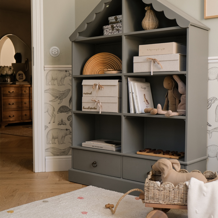 Grijze houten kast in huisvorm met dozen, boeken en knuffels in kinderkamer