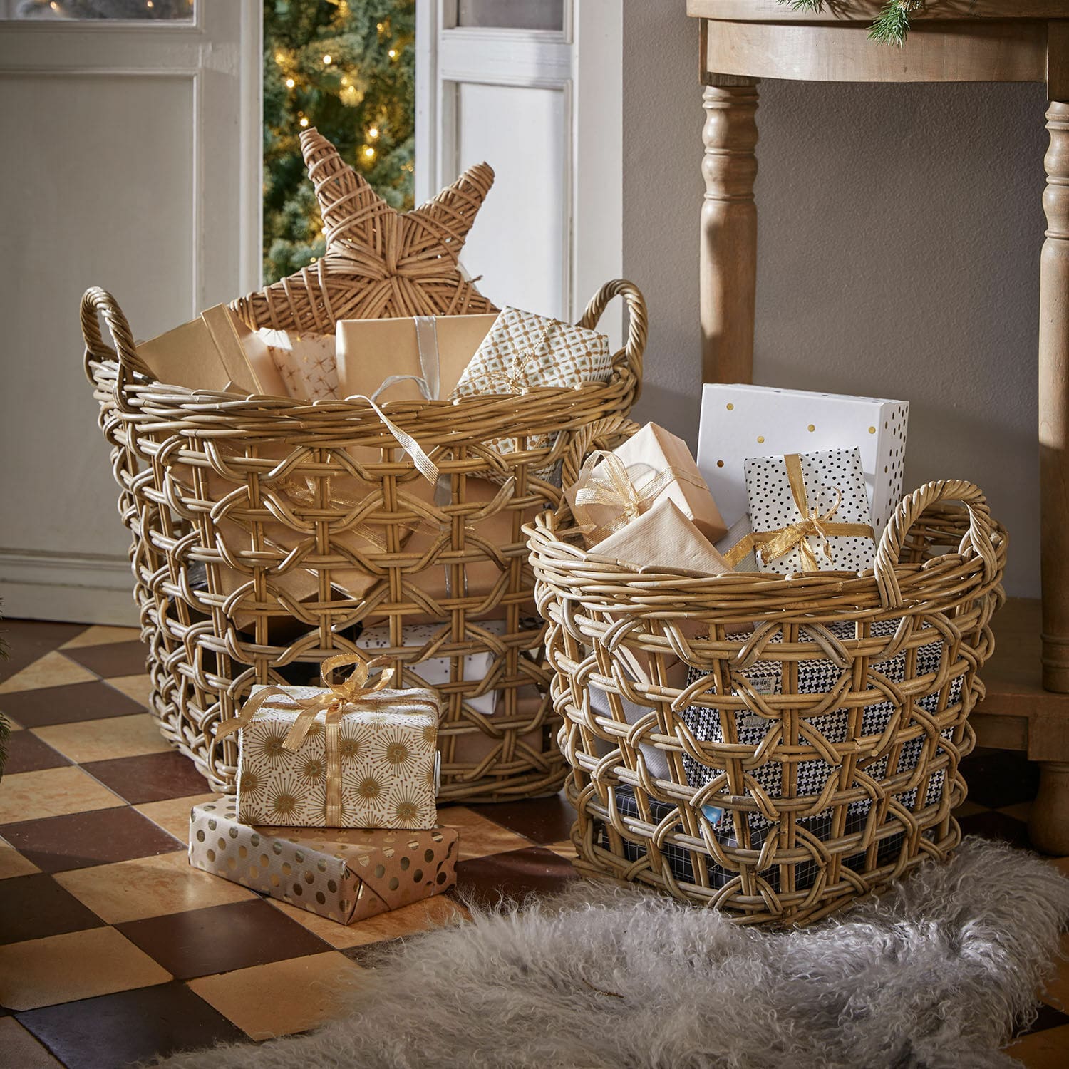 Mand set van 2 Qivoran Twee natuurlijke rieten manden met cadeaus en kerstdecoraties op een betegelde vloer.