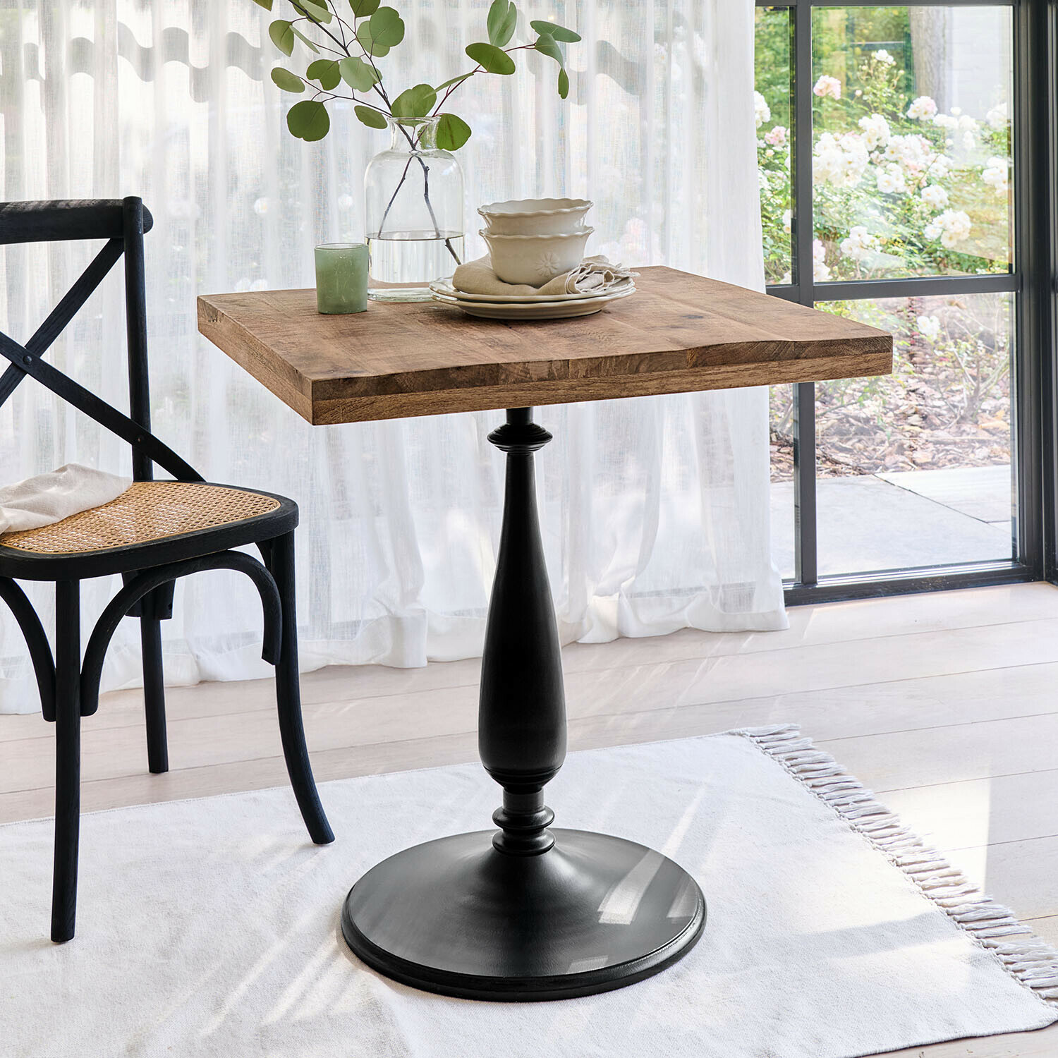 Vierkante tafel met houten blad en zwarte metalen voet in lichte kamer met stoel