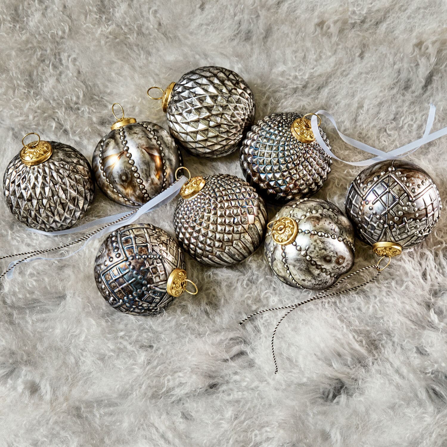 Set zilveren kerstballen met decoratieve patronen en gouden ophangingen op zachte bont