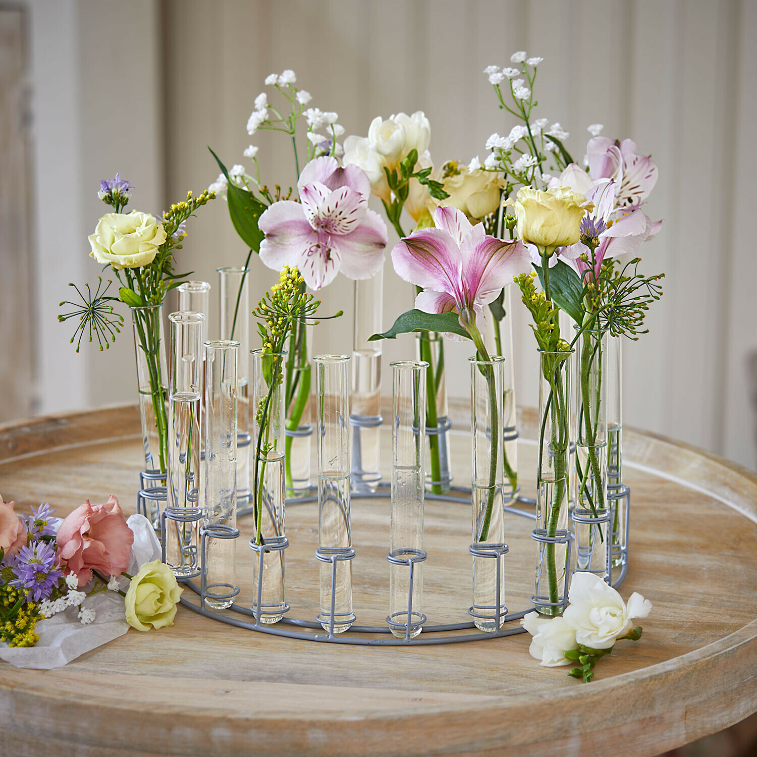 Ronde metalen krans met transparante glazen buisjes en pastelkleurige bloemen op houten tafel