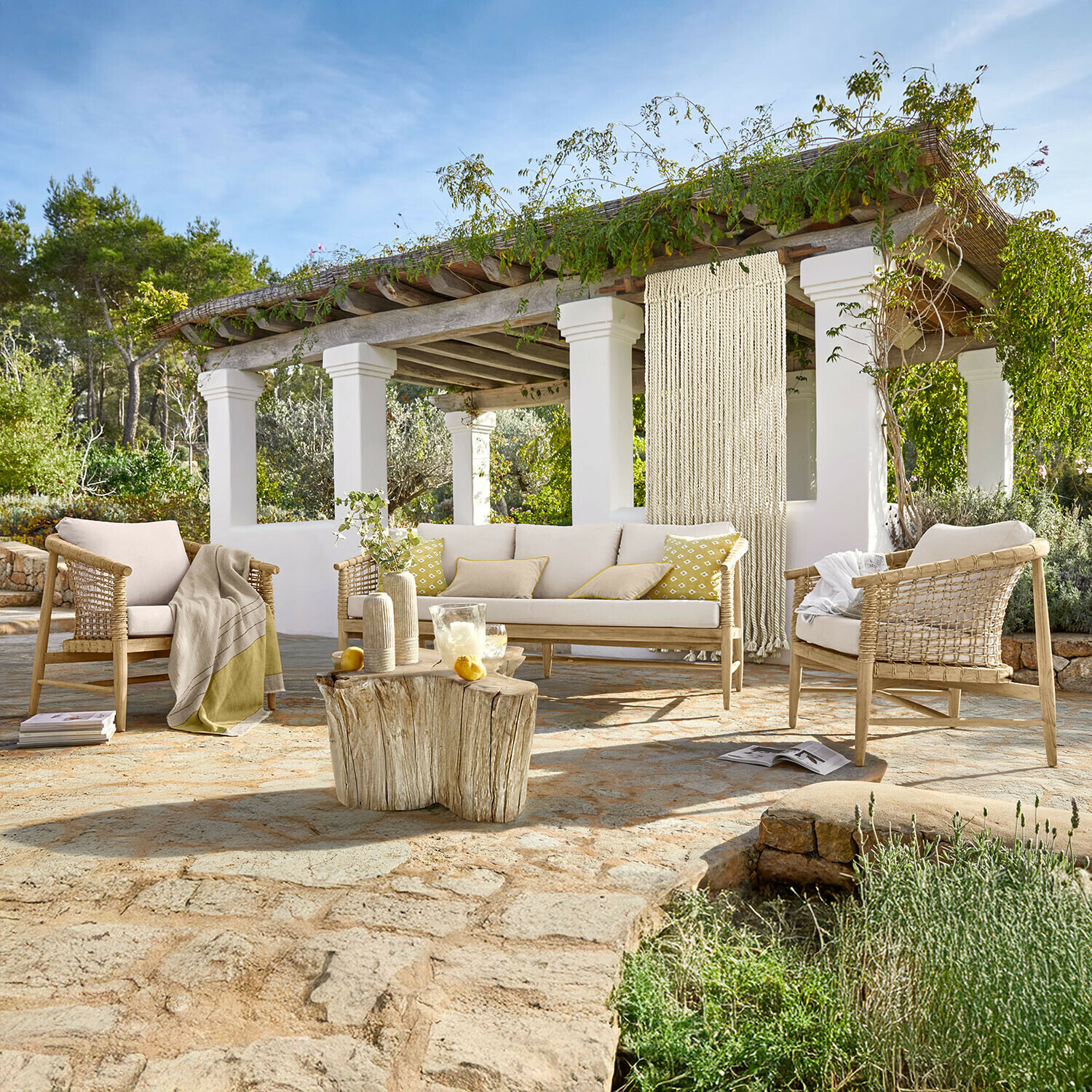 Tuinmeubelset van licht hout met beige kussens op stenen terras met natuurlijke houten tafel