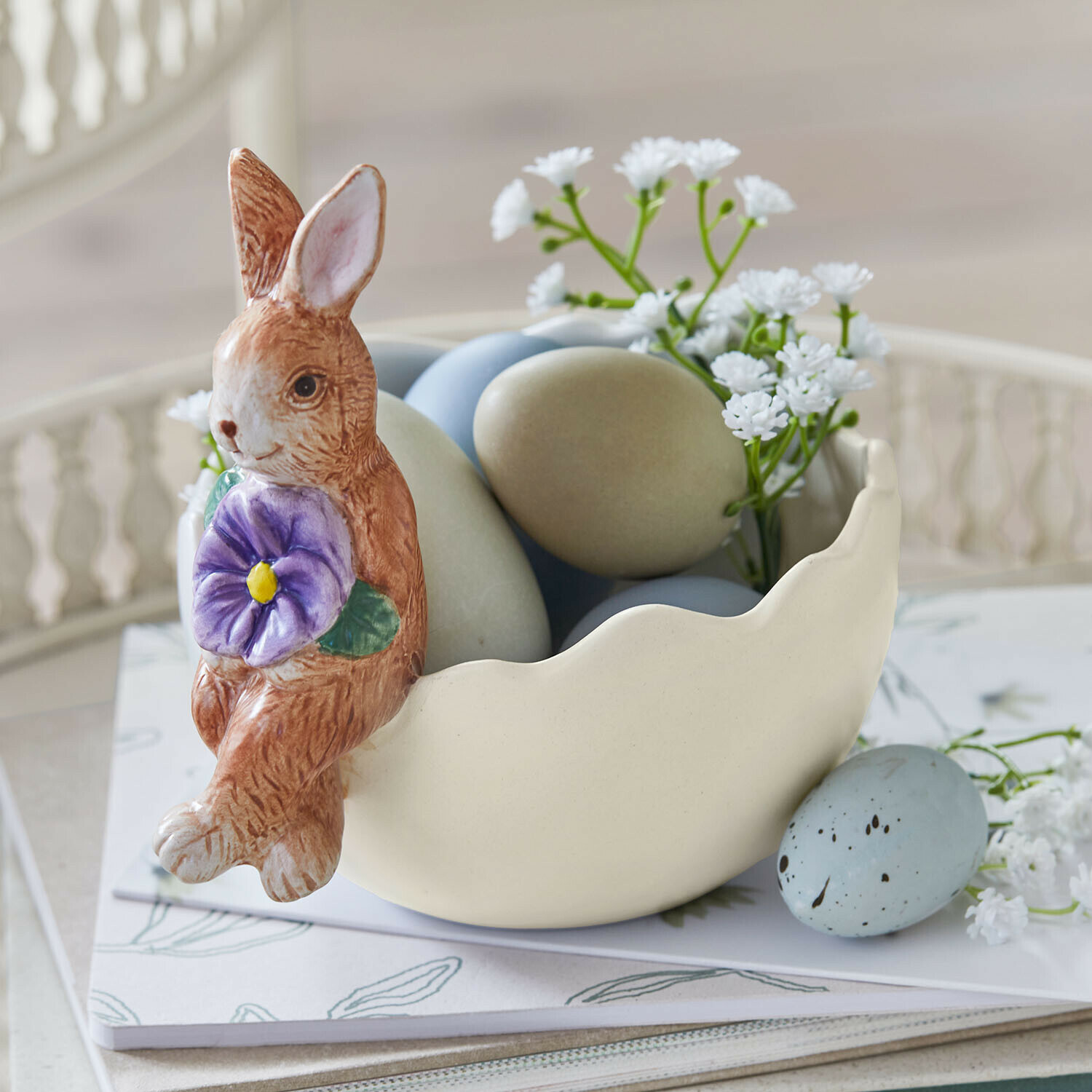 Keramische schaal met konijn, pastelkleurige eieren en witte bloemen voor lentetafeldecoratie