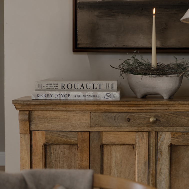 Houten dressoir met twee boeken en brandende kaars in keramische schaal op decoratieve tafel
