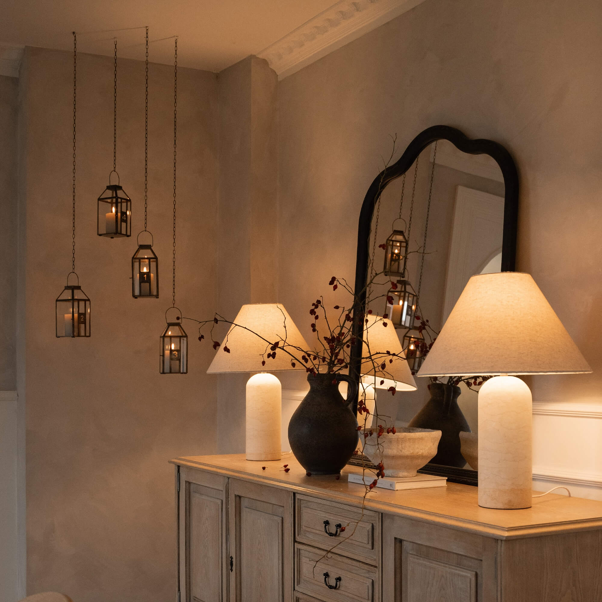 Decoratieve adventskrans met metalen lantaarns en lamp op houten dressoir in warme kamer