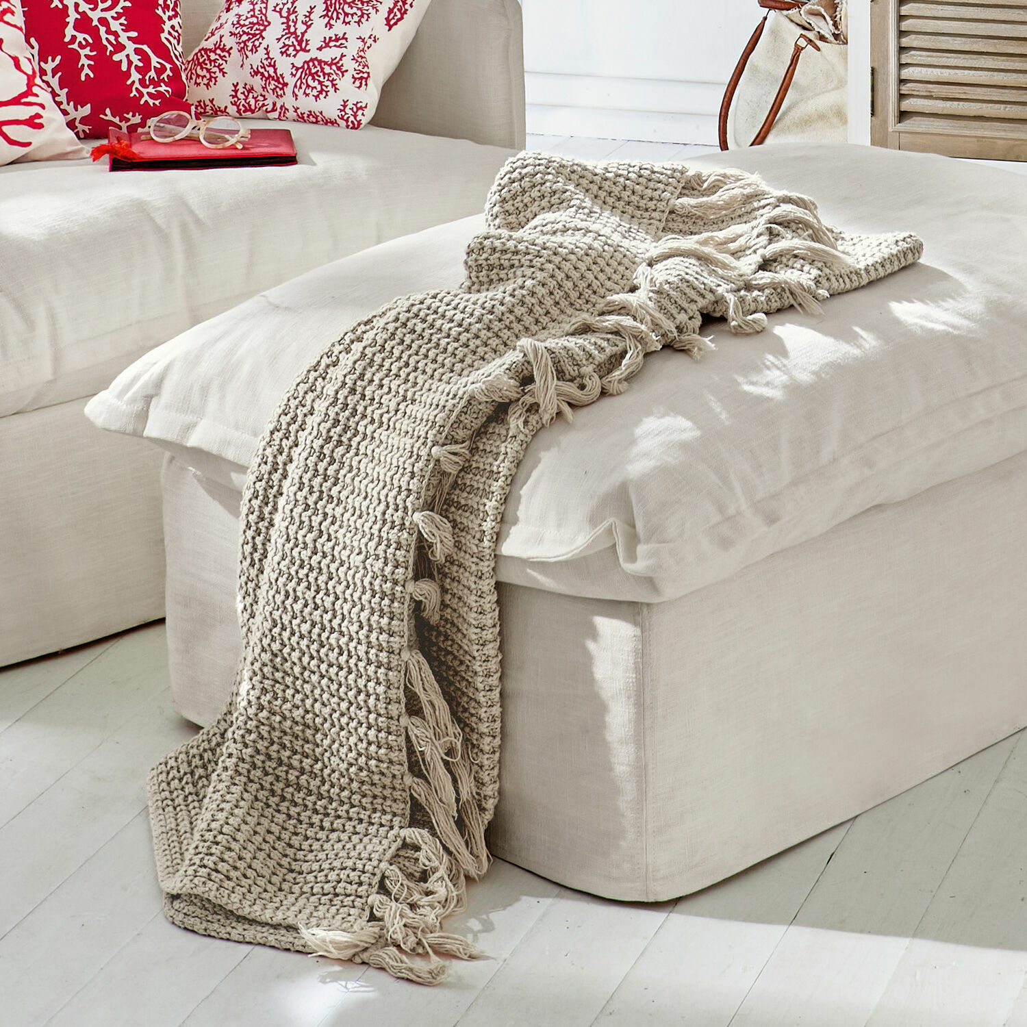 Beige gebreide deken met franjes op een lichte poef in een moderne woonkamer