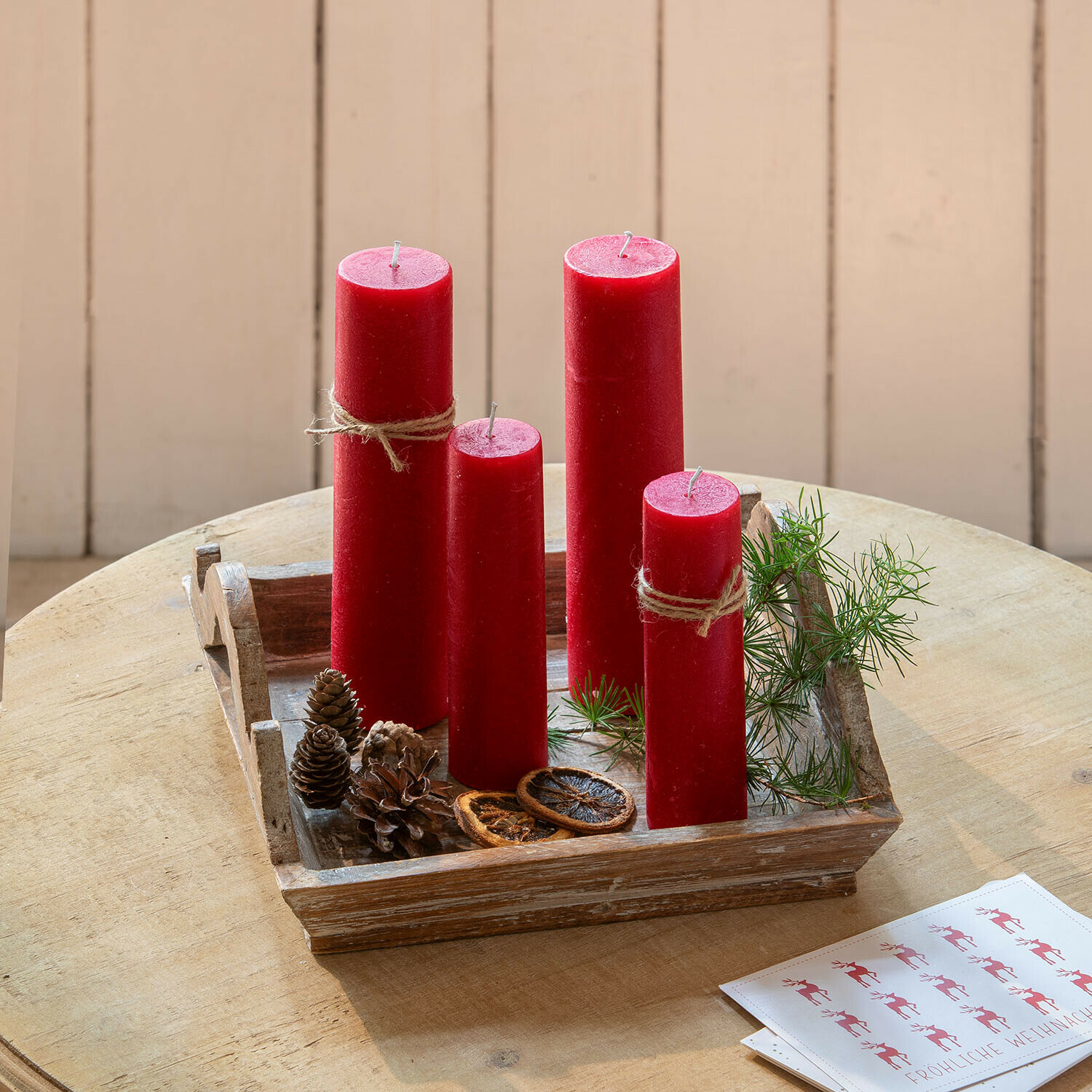 Rode kaarsen van was op een houten dienblad met natuurlijke decoraties en groene takken