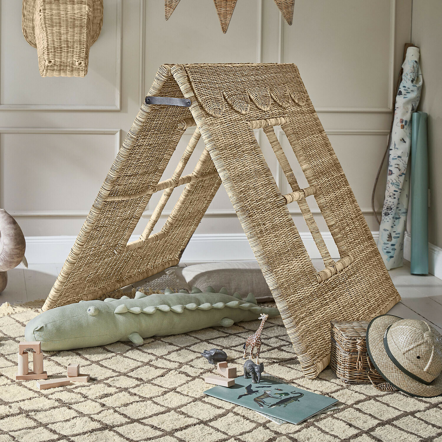 Kinderhut van natuurlijk riet op tapijt met houten speelgoed en safarihoed