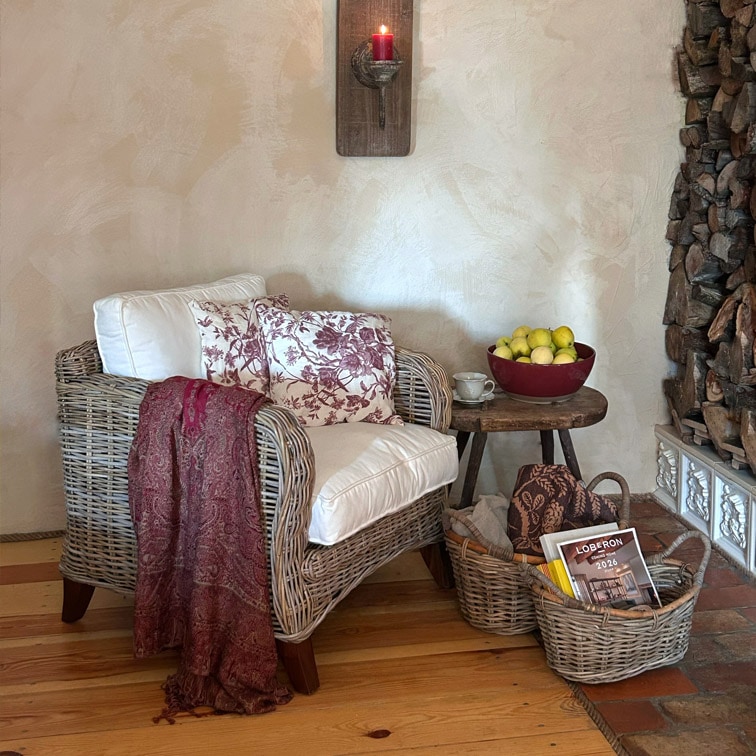 Rotan fauteuil met wit kussen en bordeauxrode deken naast houten tafel met fruitschaal en manden