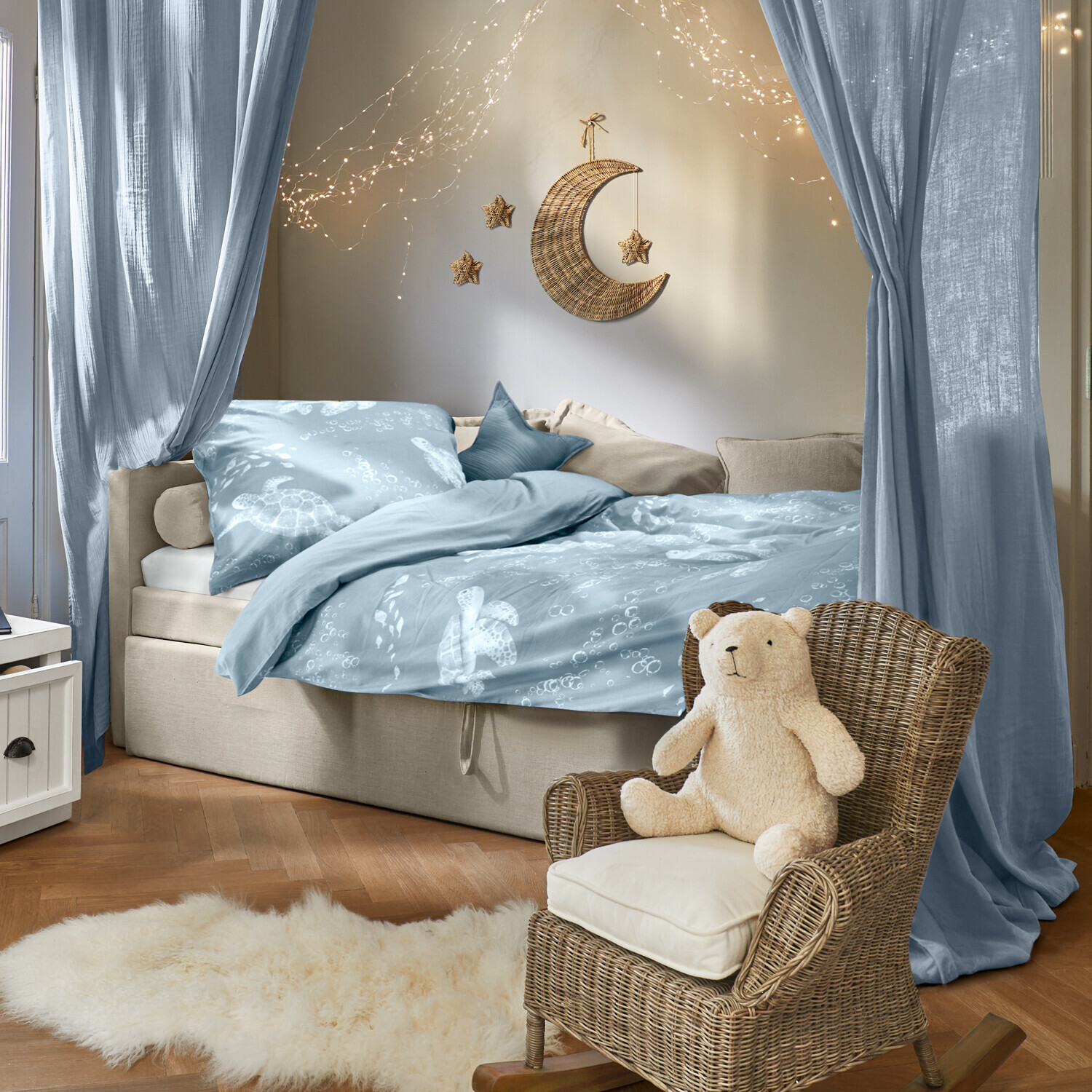 Gezellige slaapkamer met blauw beddengoed met schildpaddenmotief en rotan stoel met teddybeer