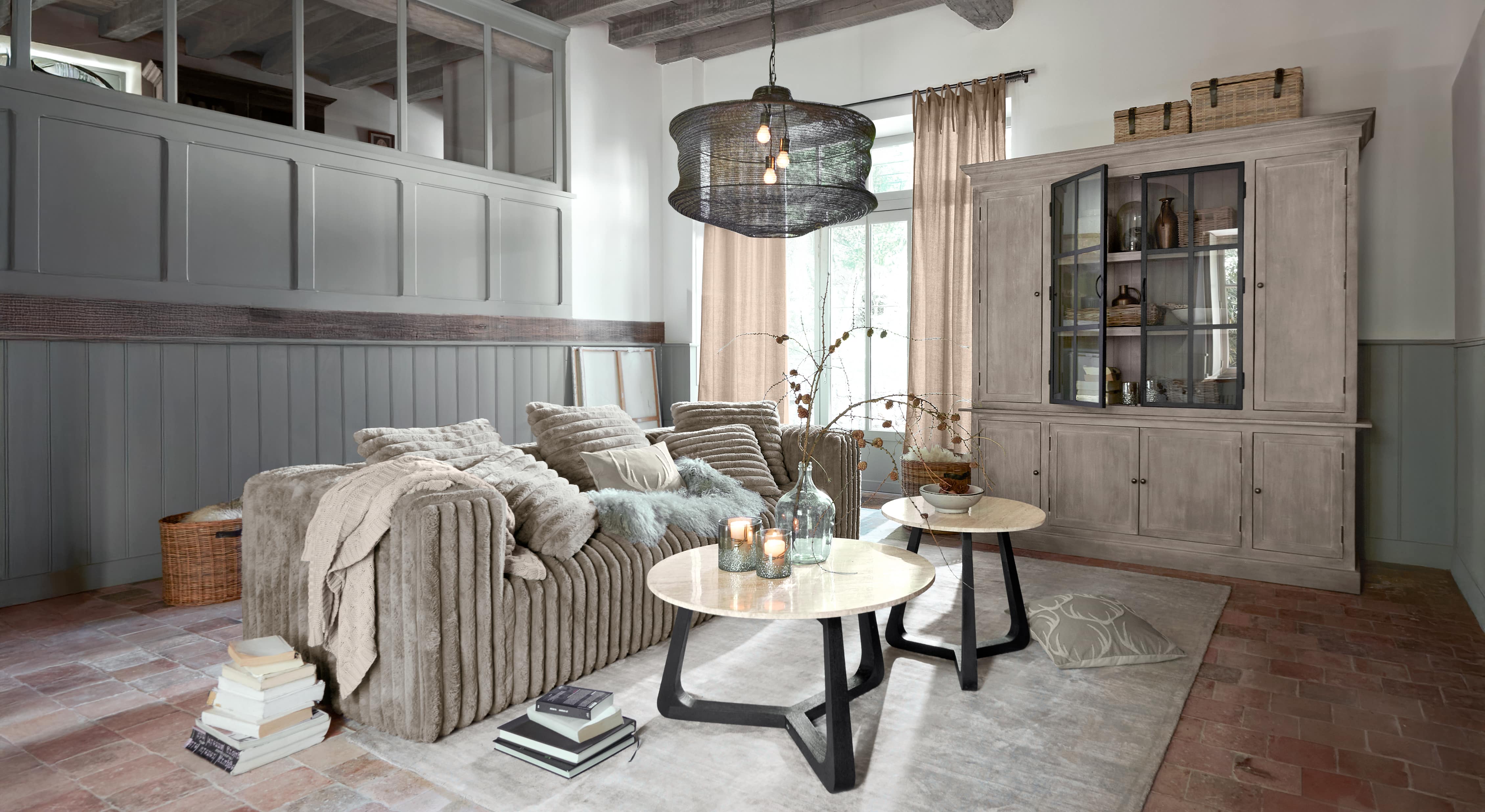 Gezellige woonkamer met beige bank van zacht materiaal en twee ronde salontafels met marmeren bladen