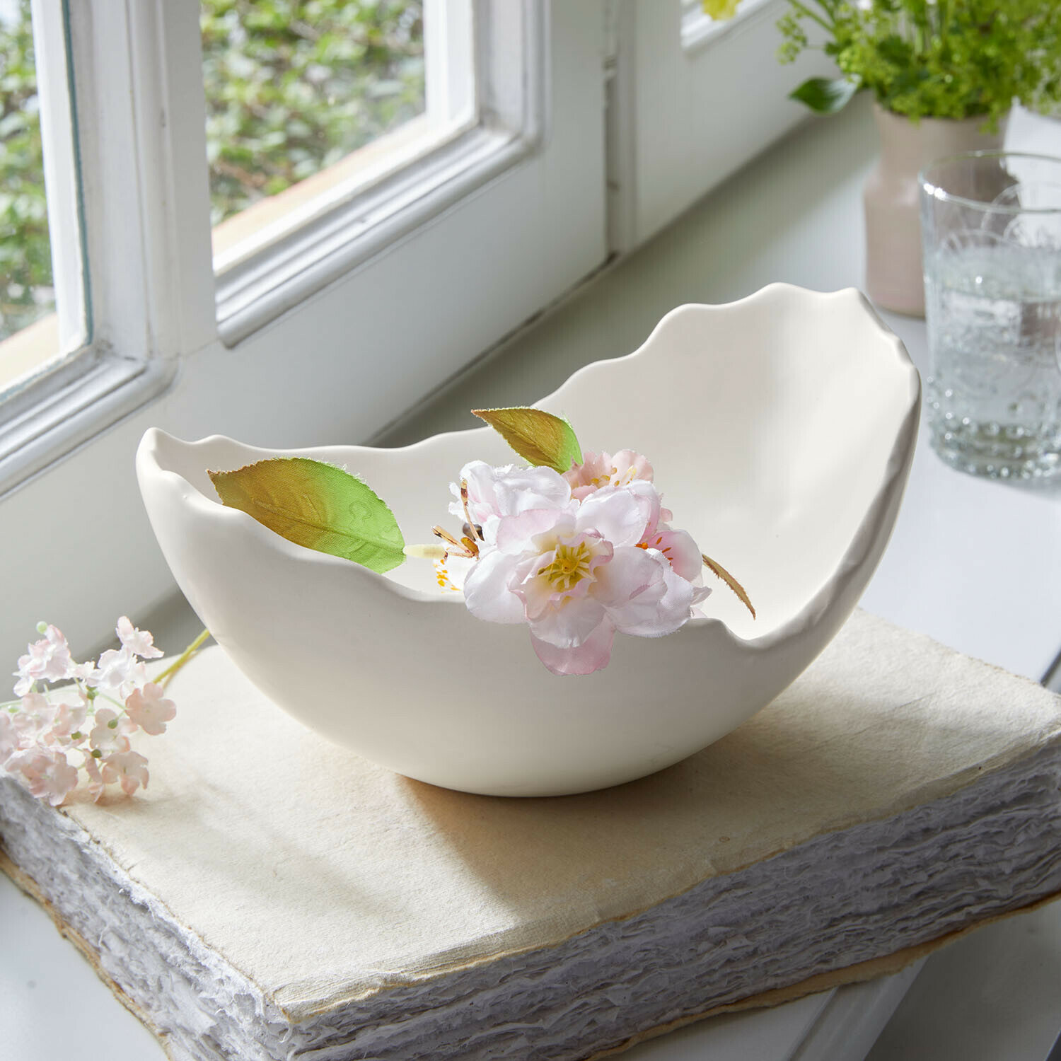 Witte keramische kom met golvende rand en delicate bloem op een boek bij het raam