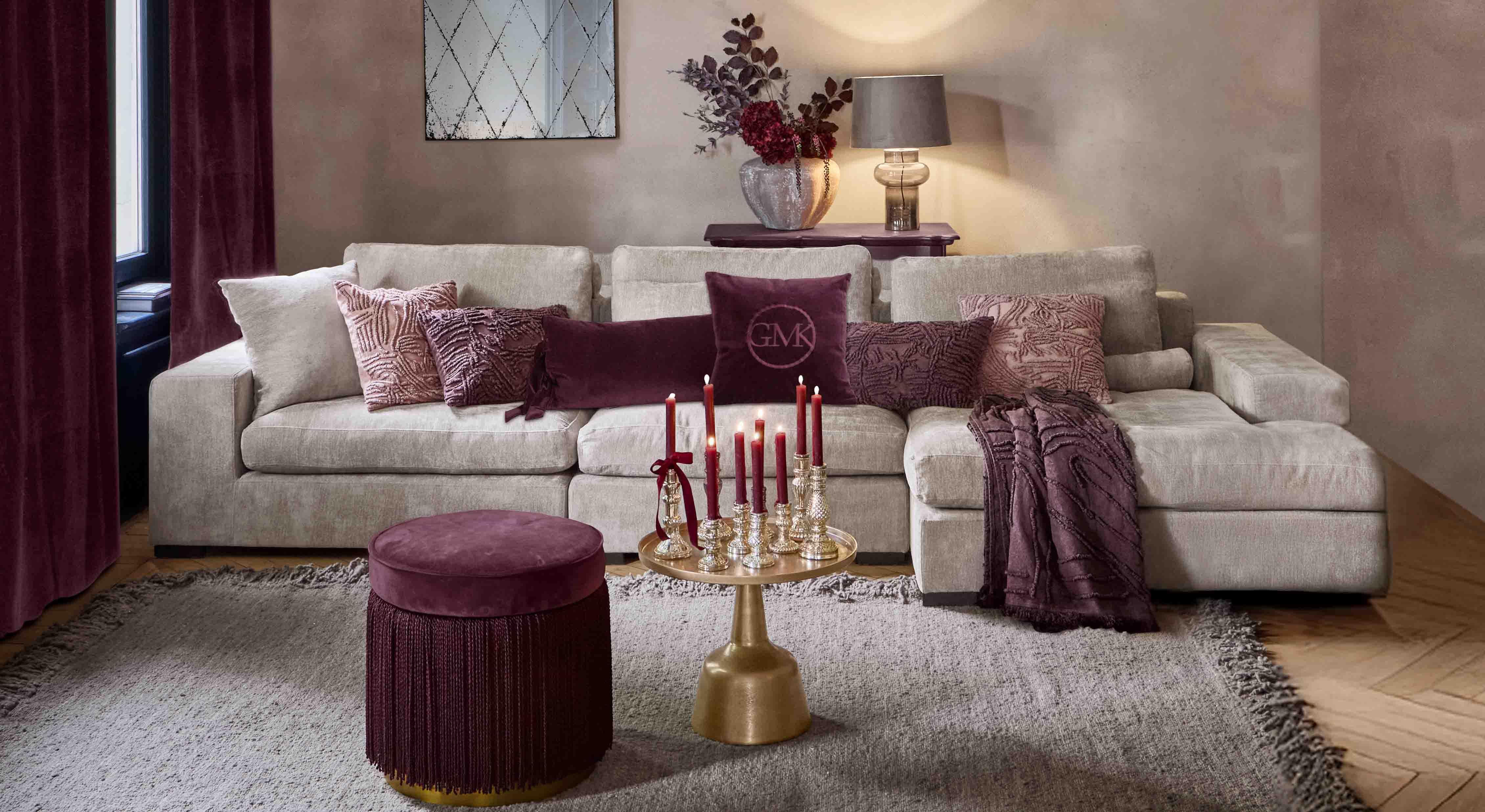 Beige bank met zachte kussens en bordeauxrode accenten in stijlvolle woonkamer met lamp en spiegel