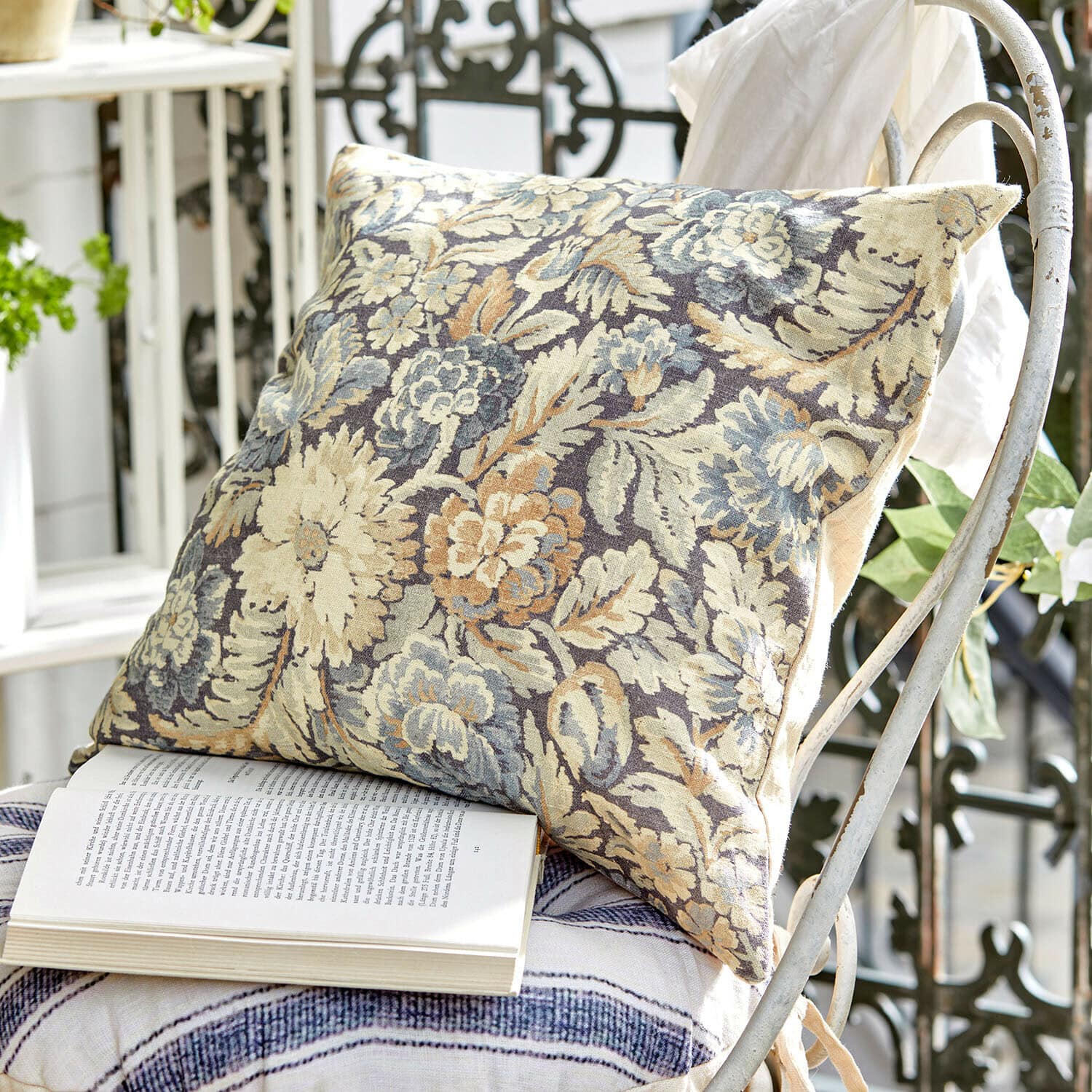 Decoratief kussen van stof met bloemenpatroon in beige en blauw op een witte metalen stoel