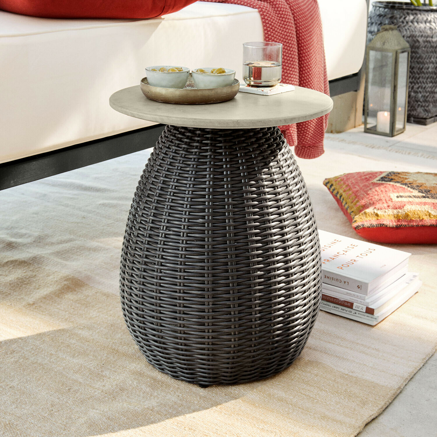 Ronde bijzettafel met grijs blad en donkergrijze gevlochten basis op een vloerkleed in woonkamer