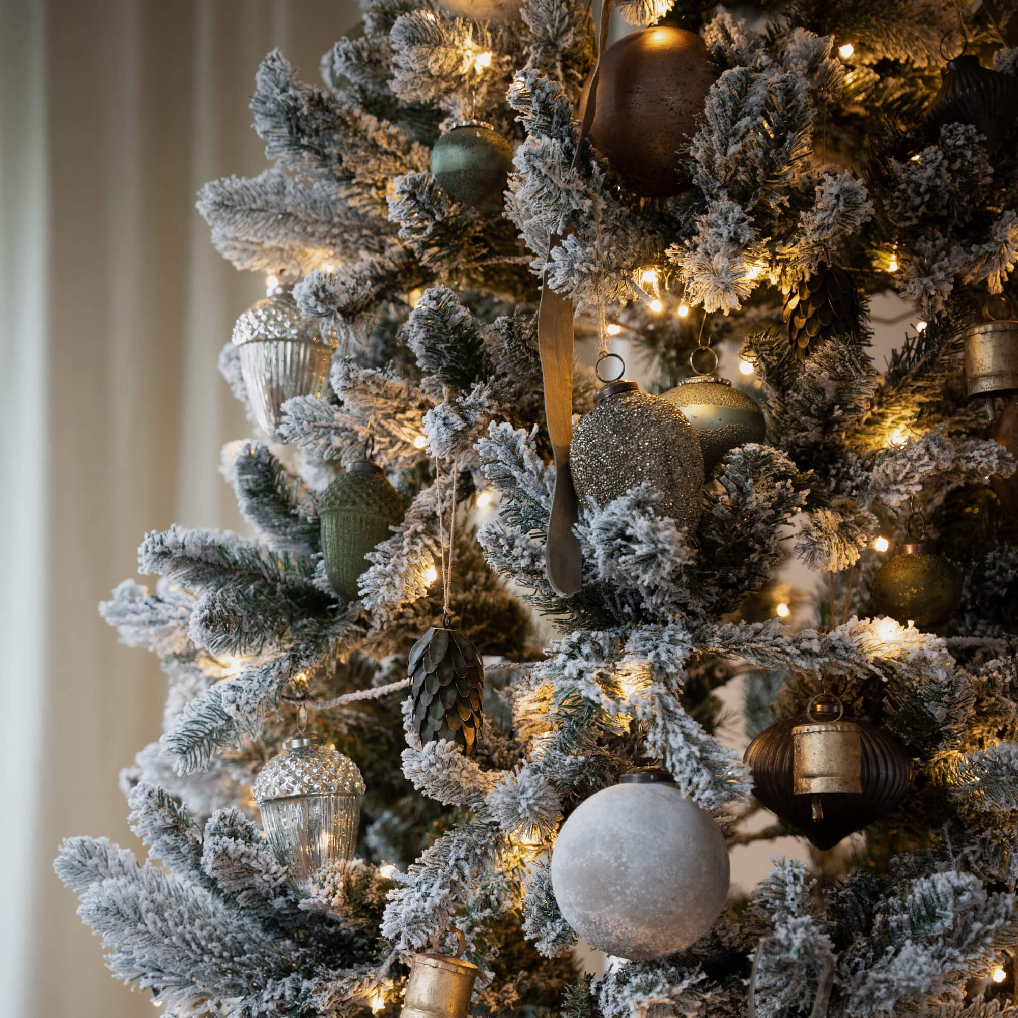 Kunstkerstboom met besneeuwde takken, gouden en groene versieringen en LED-lichtjes