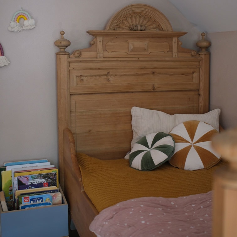 Massief houten bed met sierlijk hoofdeinde, decoratieve kussens en boeken in kinderkamer