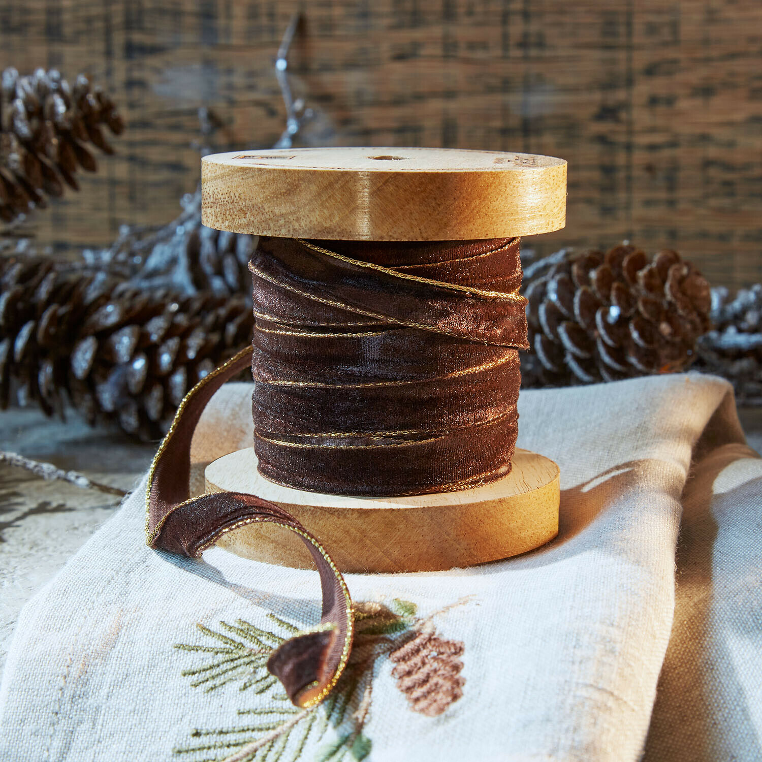Fluwelen lint Sorima Bruine fluwelen lint met gouden rand op houten spoel, feestelijke decoratie met dennenappels