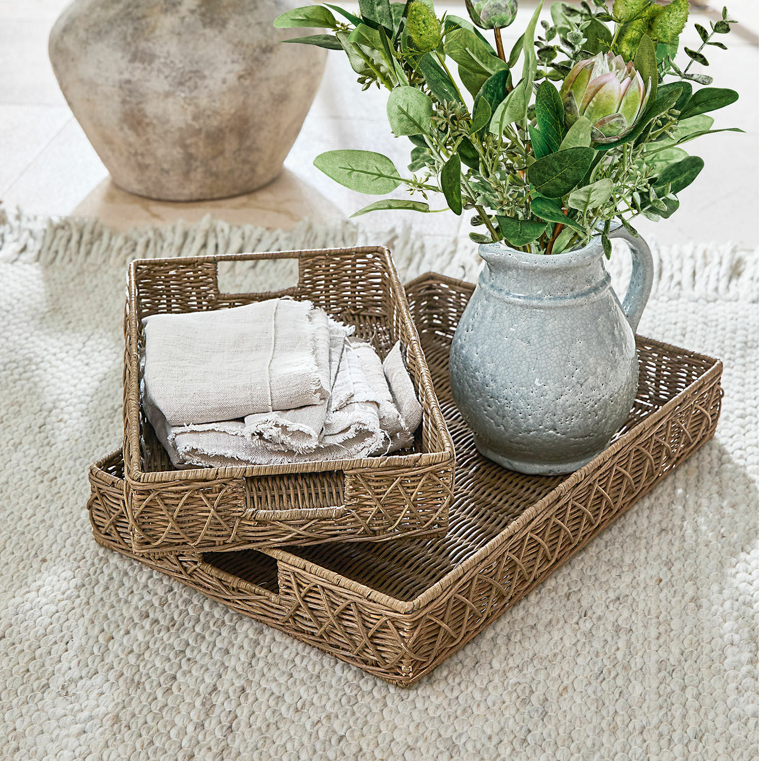 Set van twee natuurlijke rieten dienbladen met grijze keramische kan en groen boeket