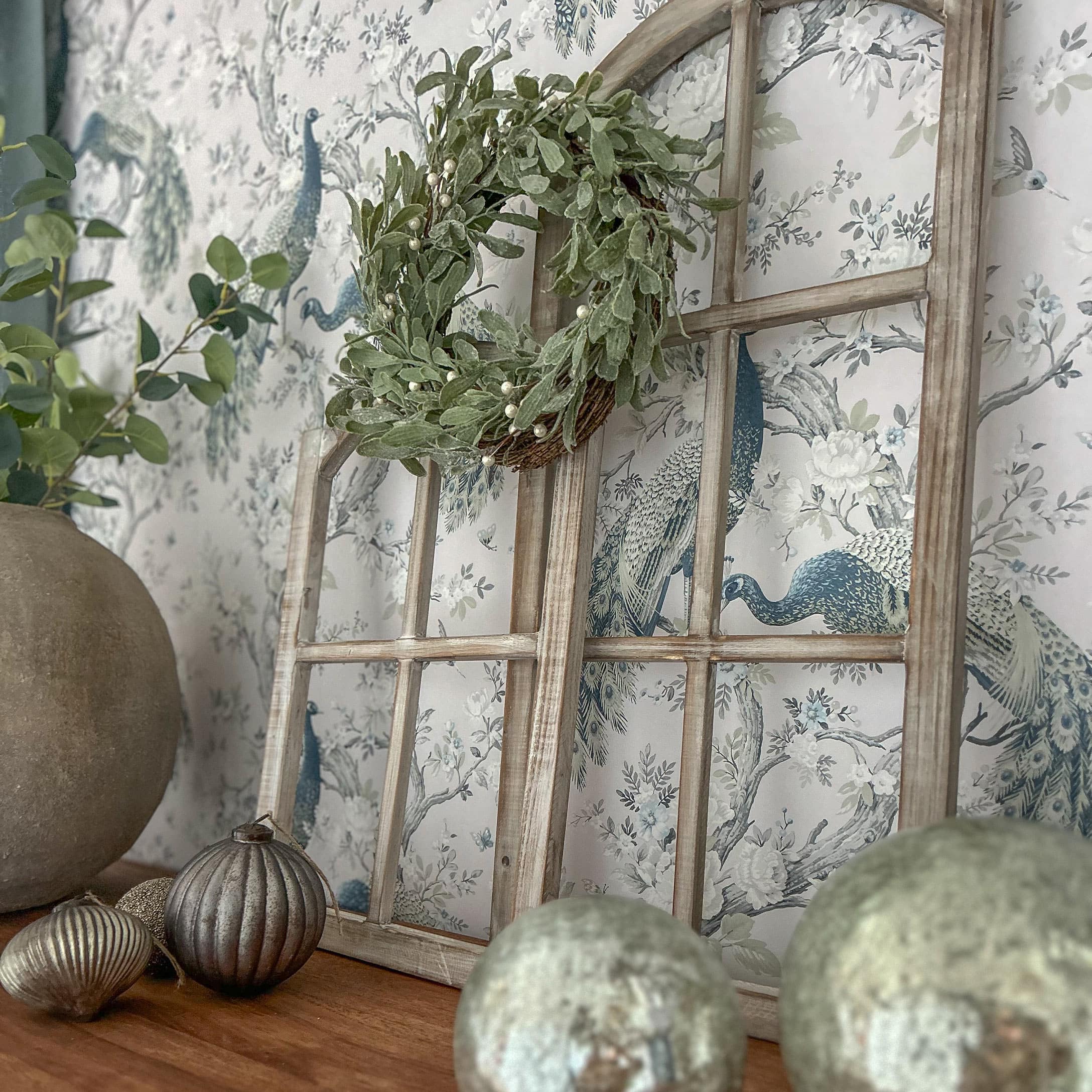 Decoratief houten raamkozijn met groene krans en metalen ornamenten op houten tafel