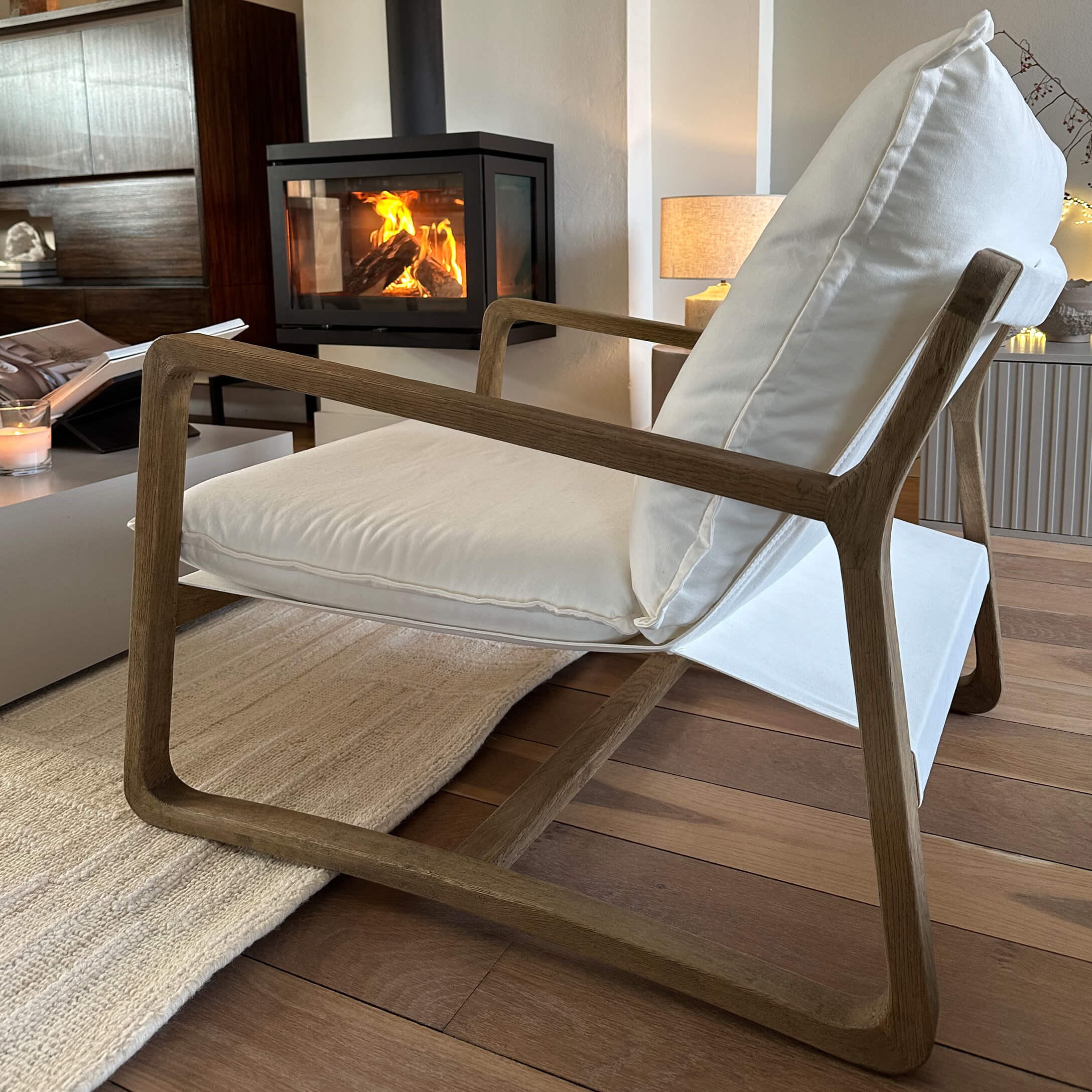 Moderne stoel met houten frame en witte stof in een gezellige woonkamer met brandende open haard