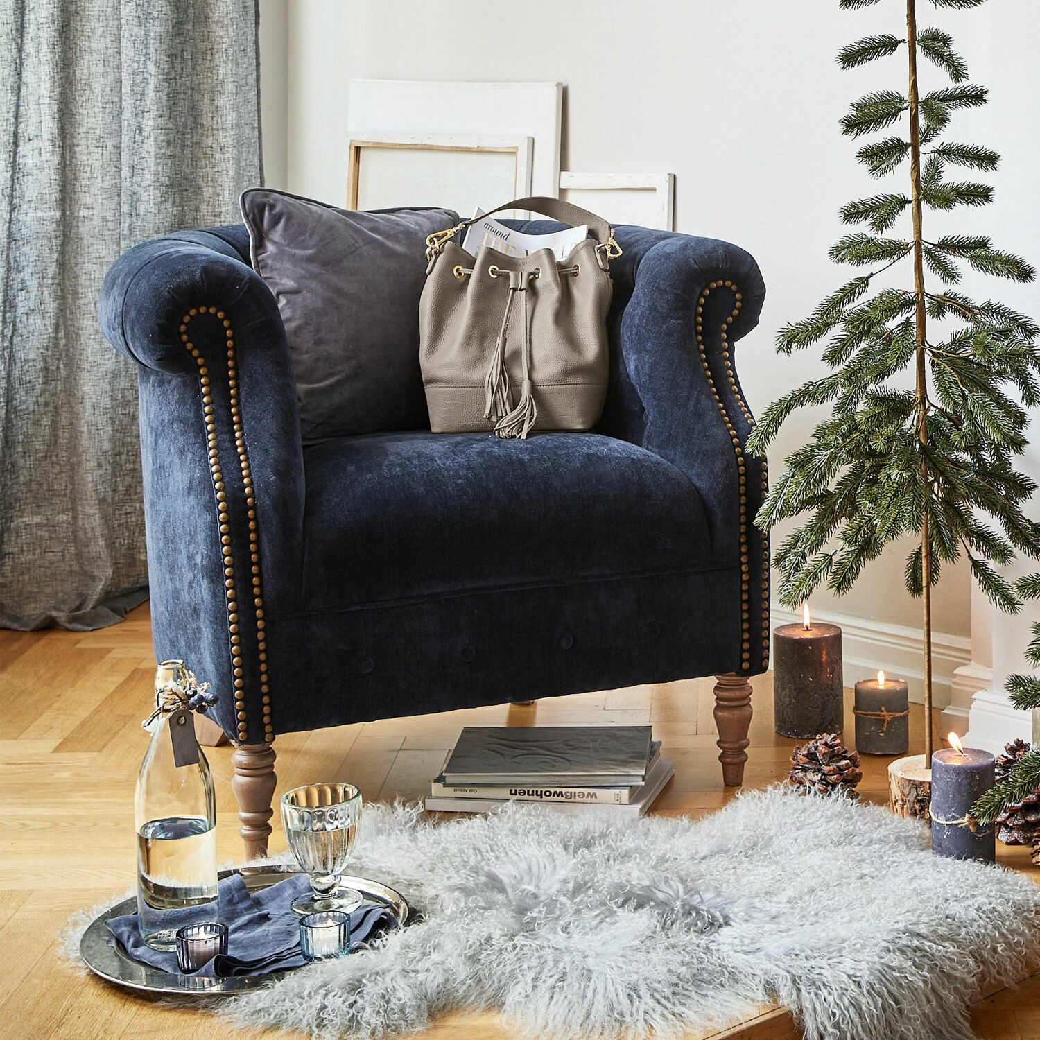 Donkerblauwe fluwelen fauteuil met siernagels en grijze tas op de armleuning in een gezellige ruimte