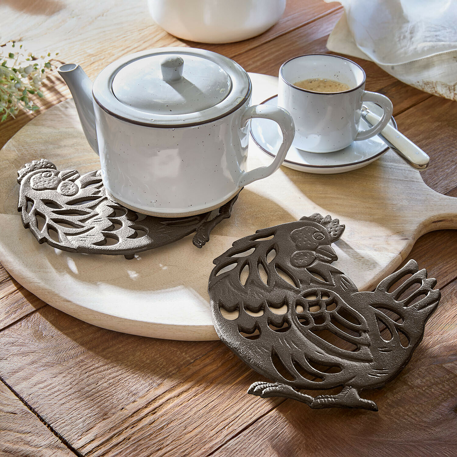 Bruine gietijzeren onderzetter in kipvorm op houten tafel met witte theepot en kopje