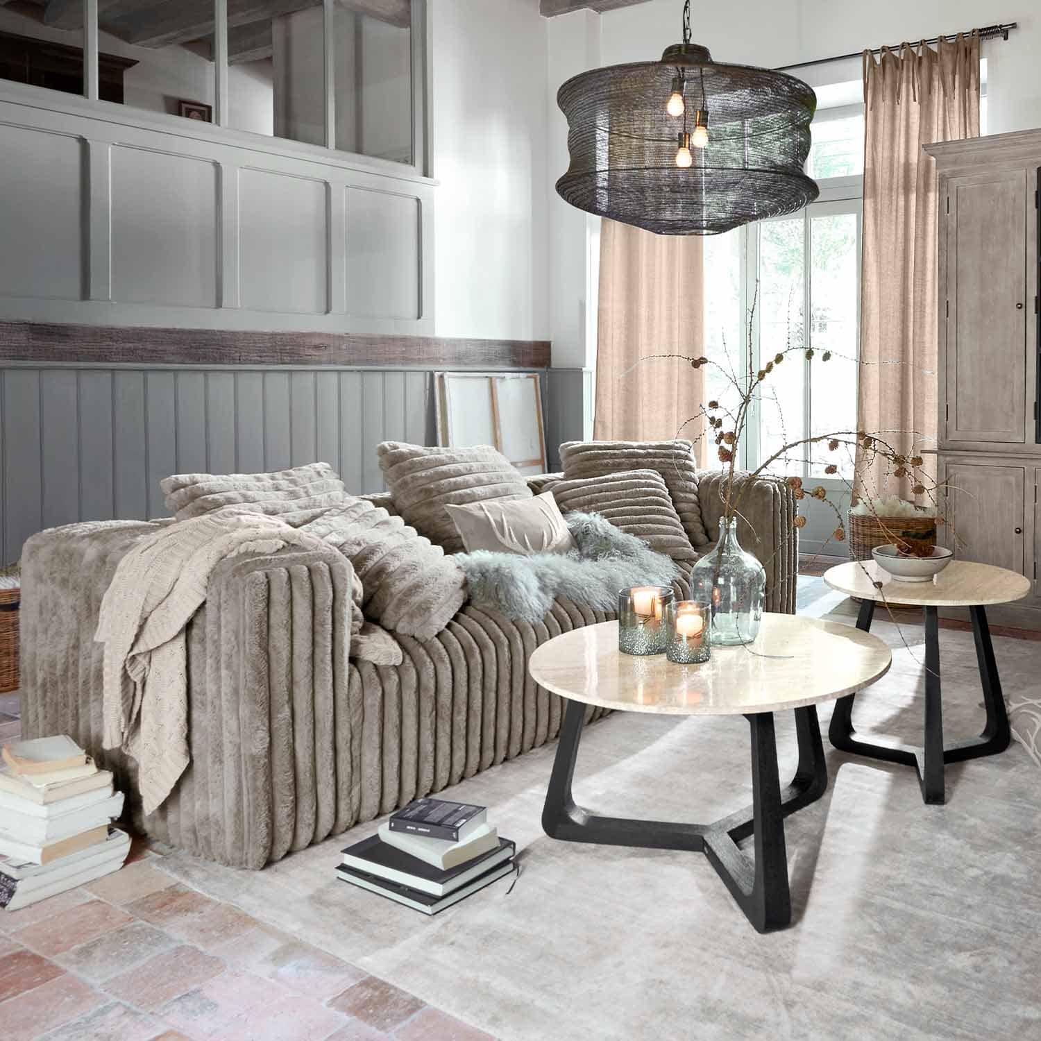 Beige zachte stoffen bank in moderne woonkamer met twee ronde salontafels van hout en metaal