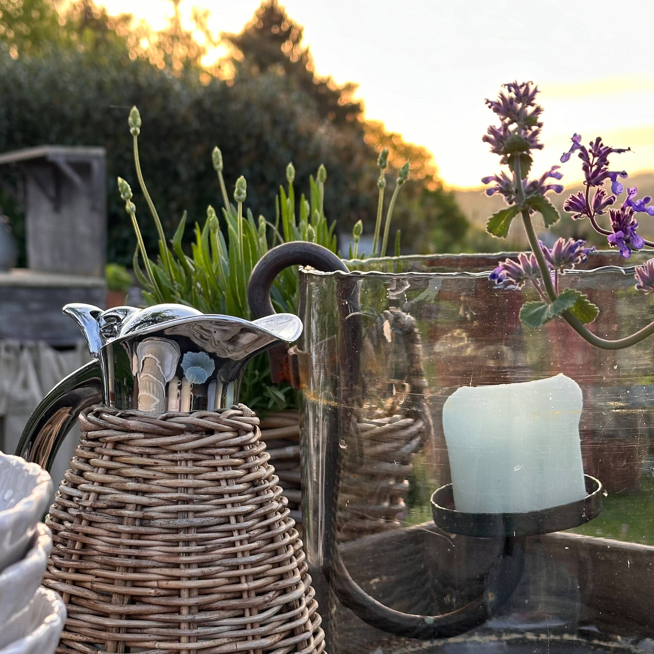 Metalen kan met rieten omhulsel en glazen kandelaar in zomerse tuin