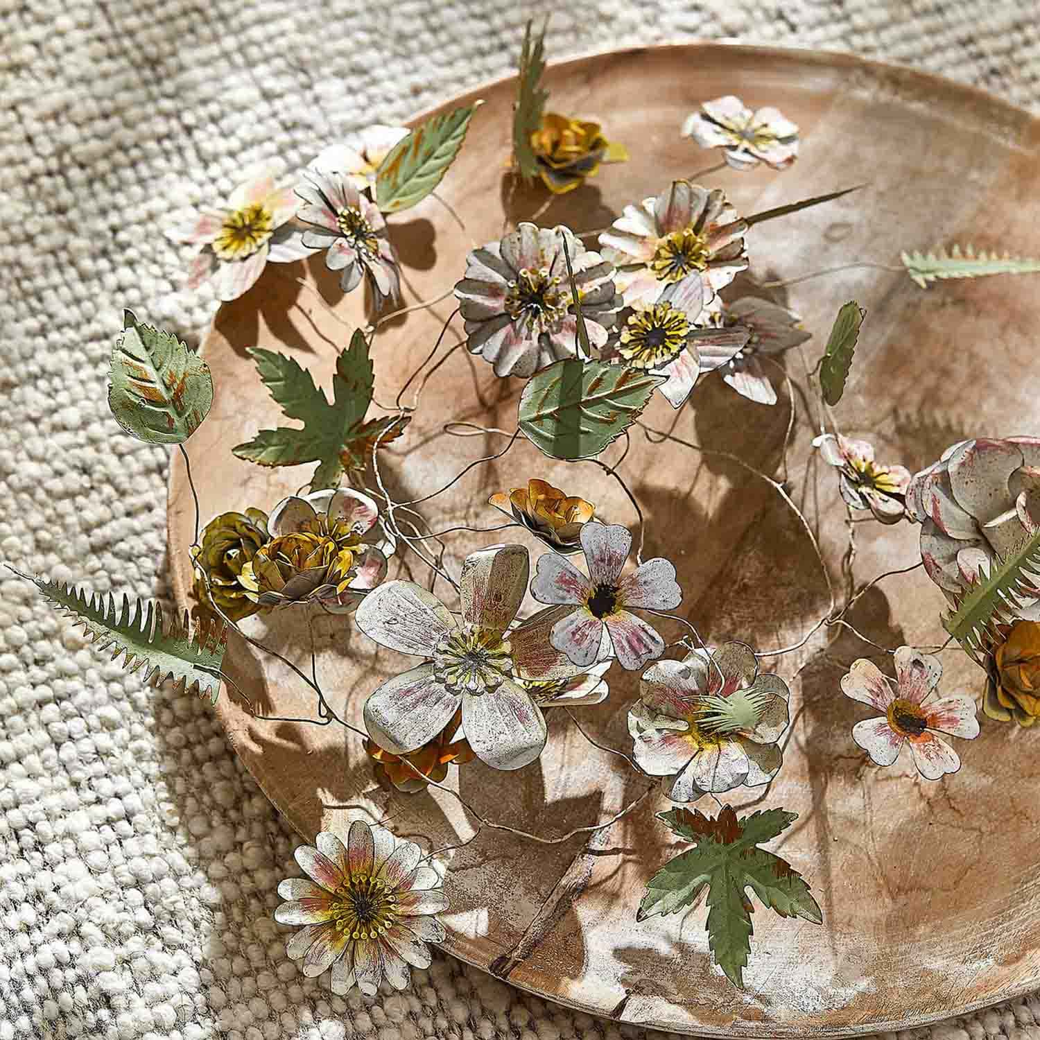 Decoratieve metalen bloemen en bladeren in natuurlijke kleuren op een houten schaal op een tapijt