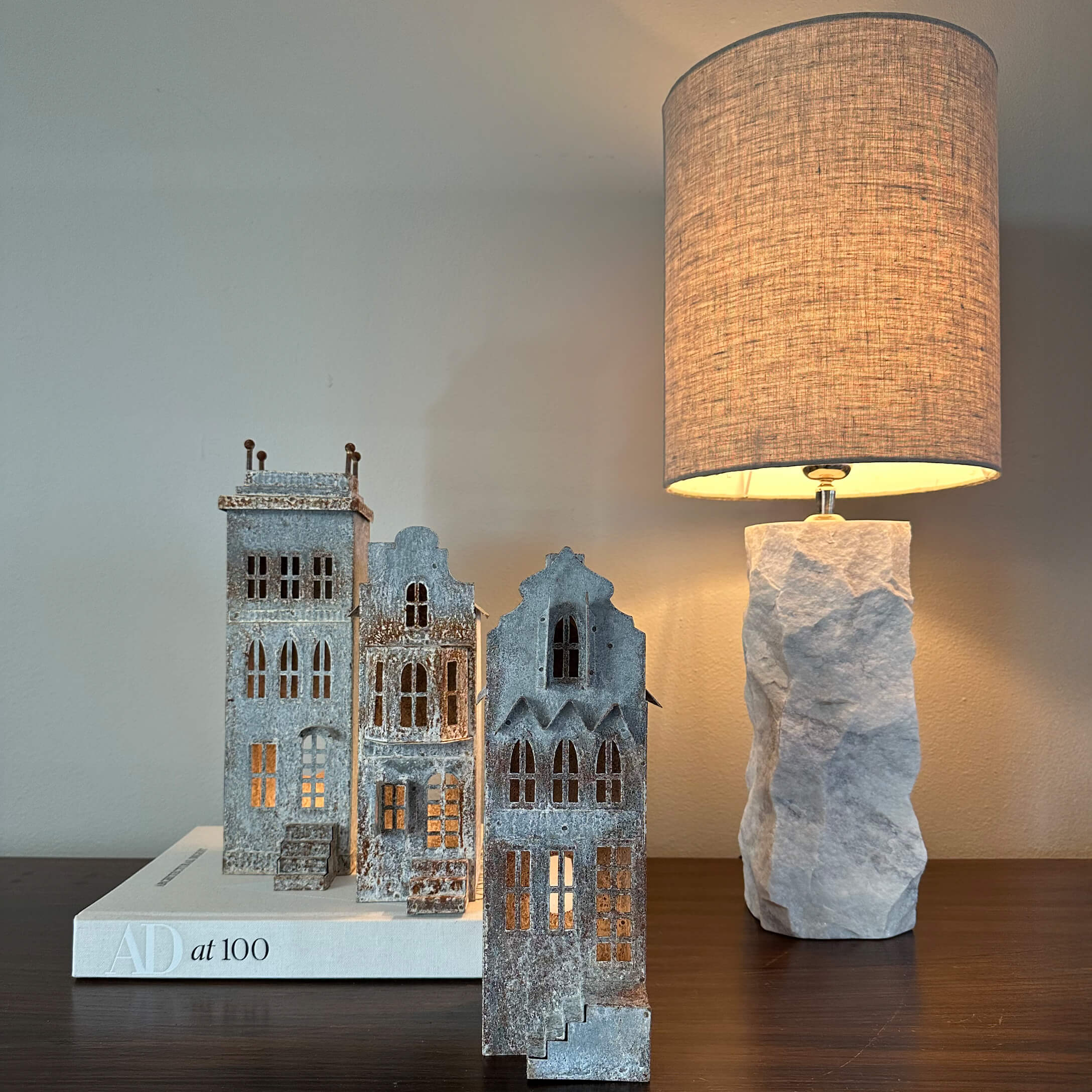 Decoratieve grijze metalen huisjes op een wit boek naast een lamp met stenen voet