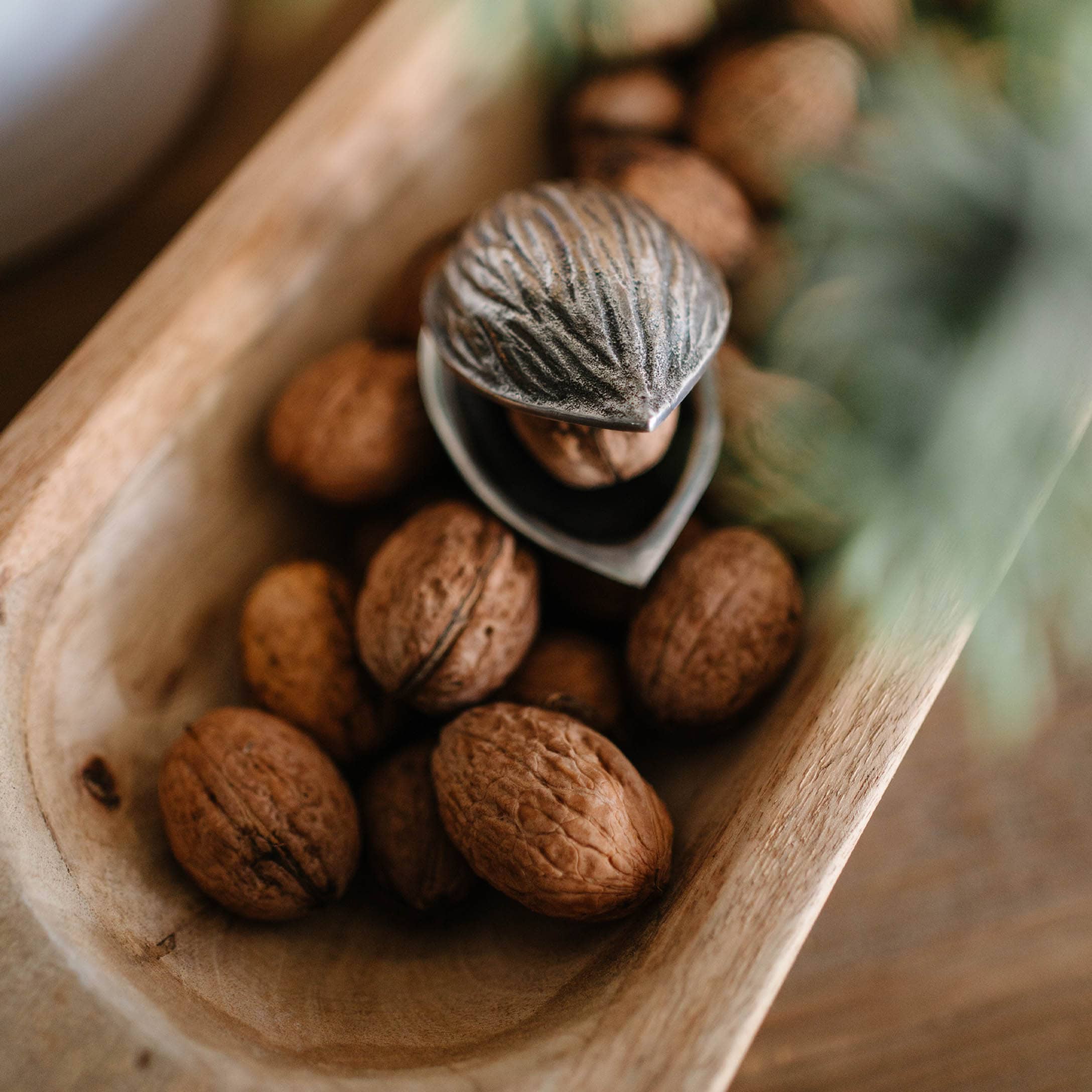 Metalen notenkraker in notenvorm op houten schaal met hele walnoten