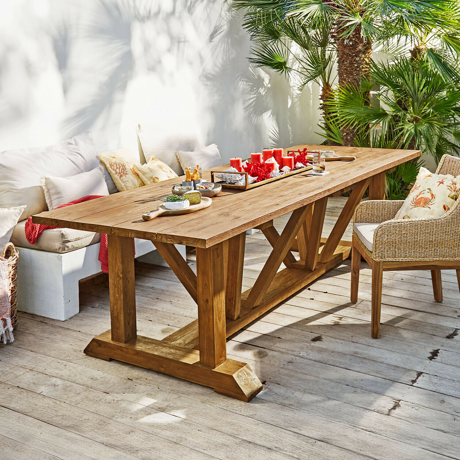 Grote eettafel van natuurlijk teakhout op terras met rode kaarsen en hapjes als decoratie