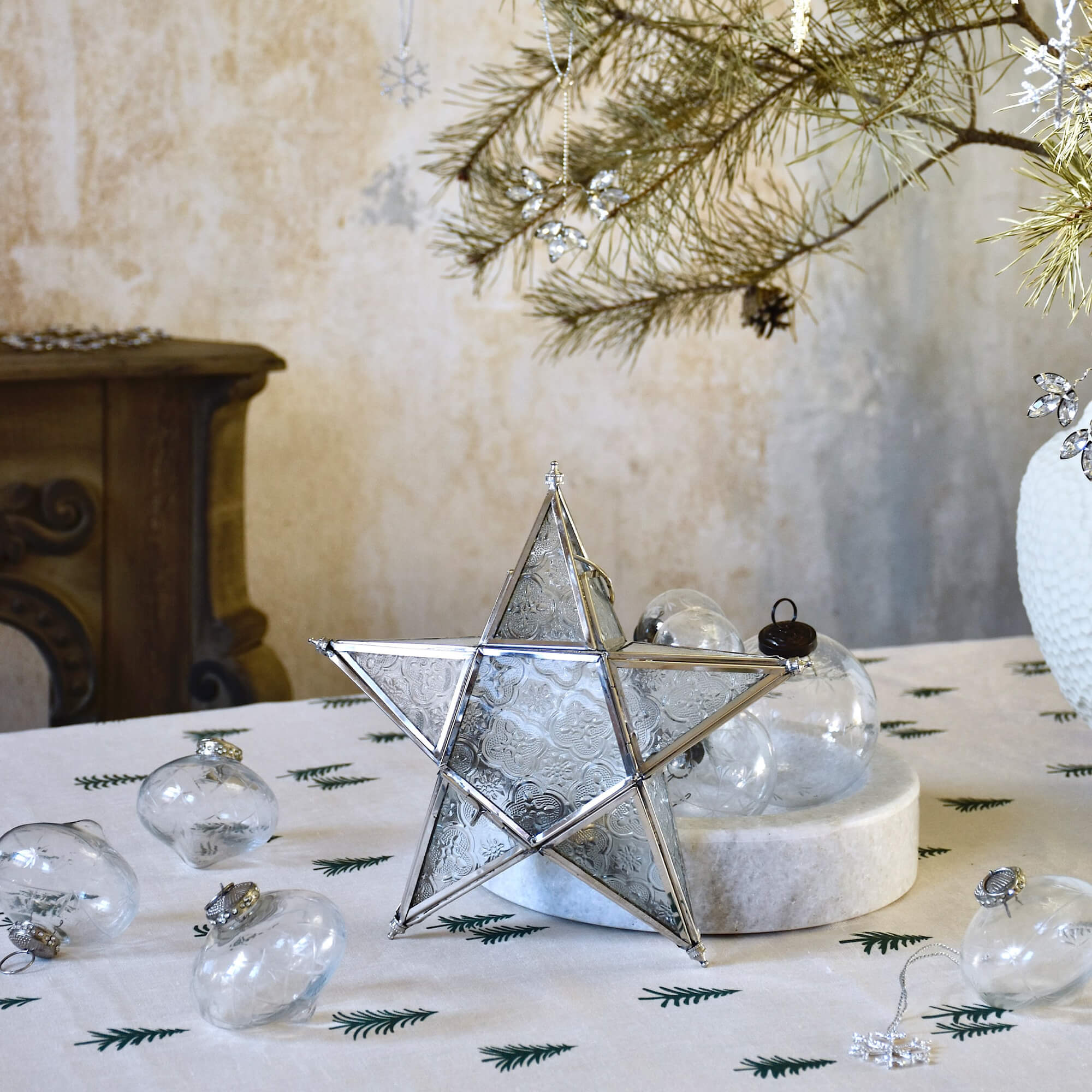 Glazen ster met metalen frame op feestelijk gedekte tafel met dennentakken en versieringen