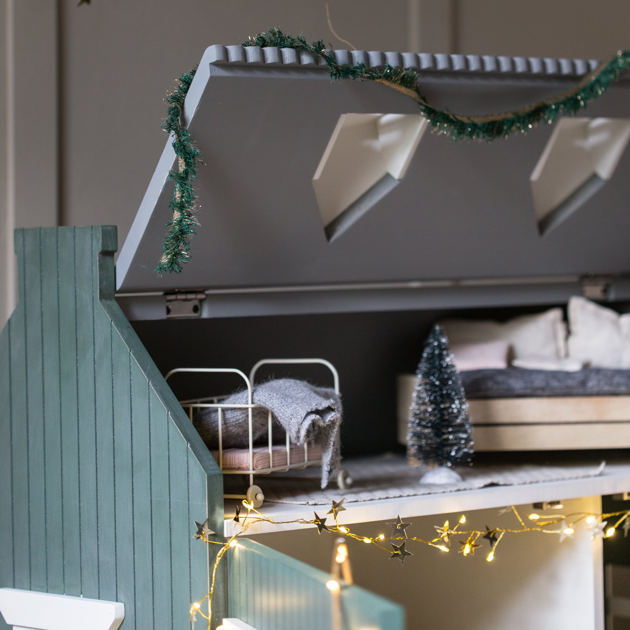 Houten poppenhuis met groen dak, miniatuurbed en decoratieve lichtslinger