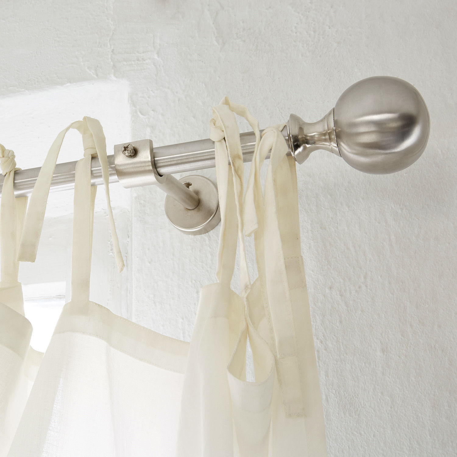 Zilverkleurige metalen gordijnroede met bolvormige eindknop en witte gordijn met linten