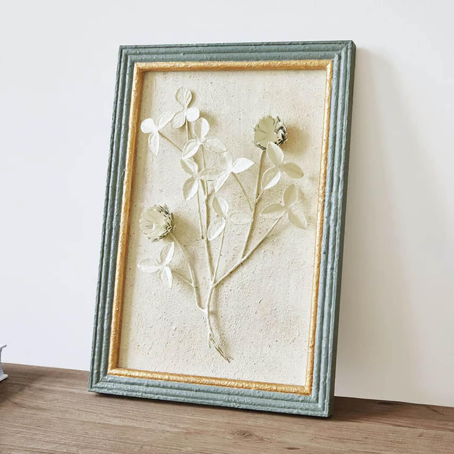 Decoratief bloemenreliëf in een groen-gouden lijst met gestructureerd oppervlak op lichte achtergrond