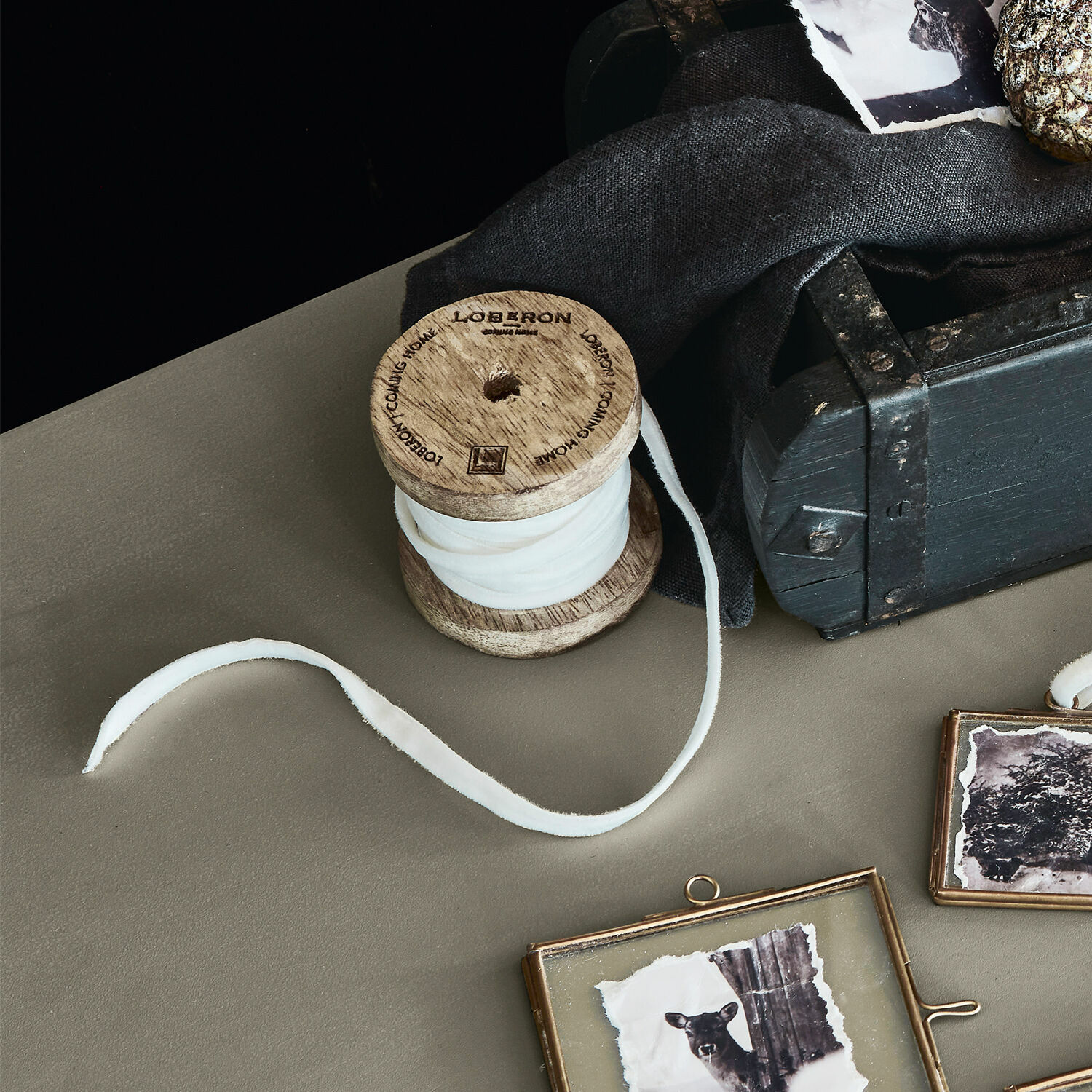 Fluwelen lint Olessa Houten spoel met witte stof op tafel naast zwarte doos en decoratieve fotolijsten