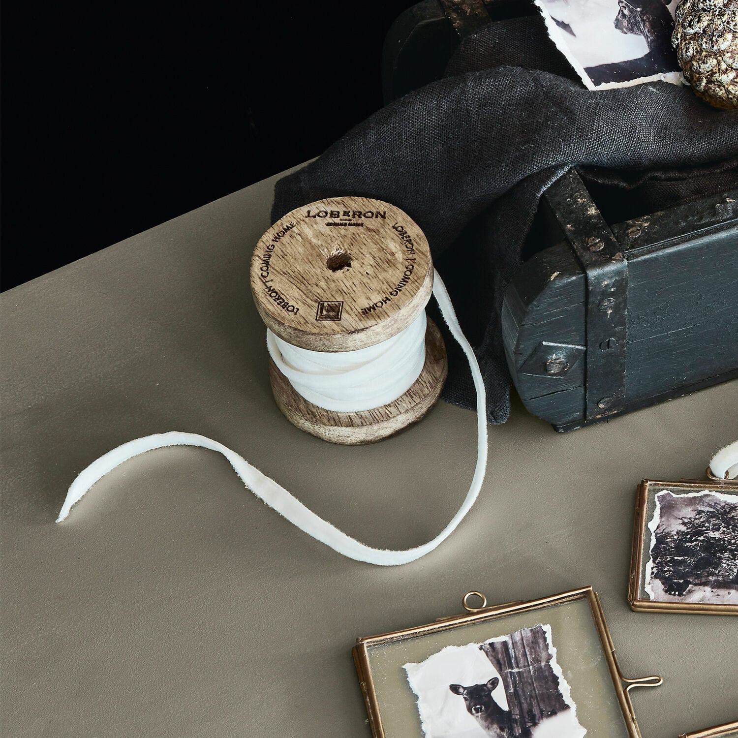 Fluwelen lint Olessa Houten spoel met witte stof op tafel naast zwarte doos en decoratieve fotolijsten