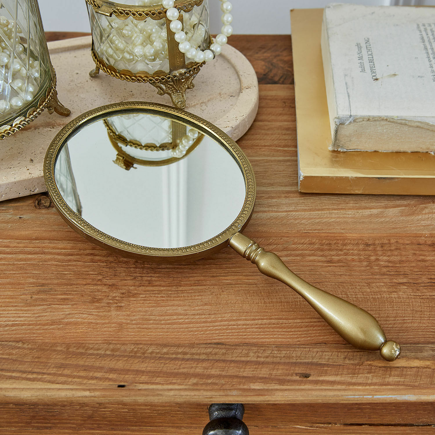 Gouden handspiegel met decoratieve rand op houten tafel met boeken en parels