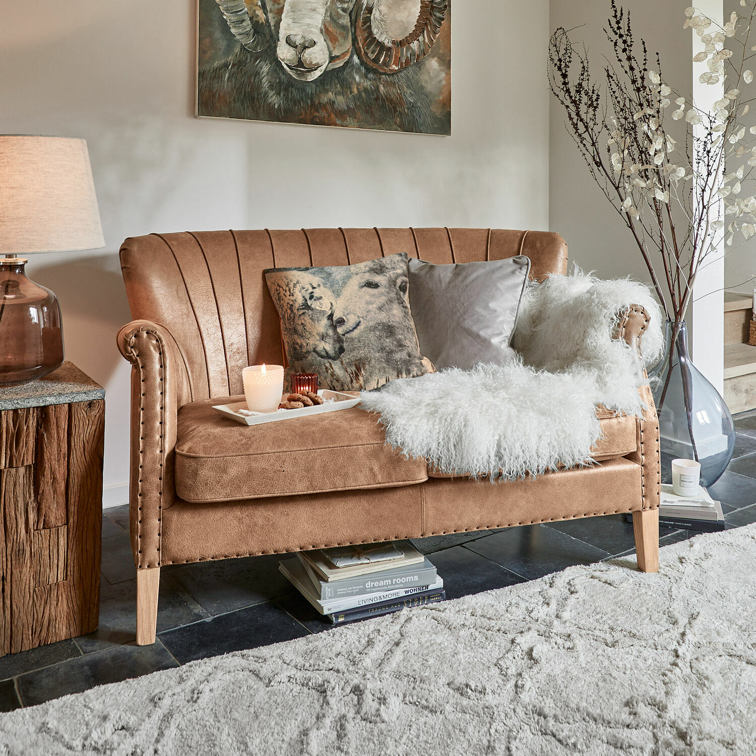 Bank Brookfield Bruine bank van zacht materiaal met decoratieve kussens en witte bontdeken in woonkamer