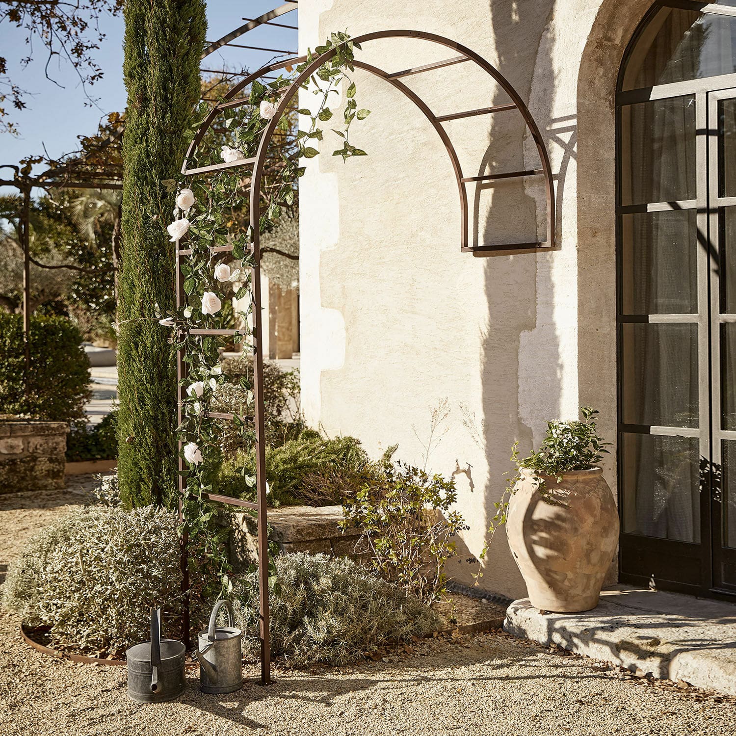 Rozenboog Auburn Bruine metalen tuinpergola met boog, witte rozen en gieters op grind