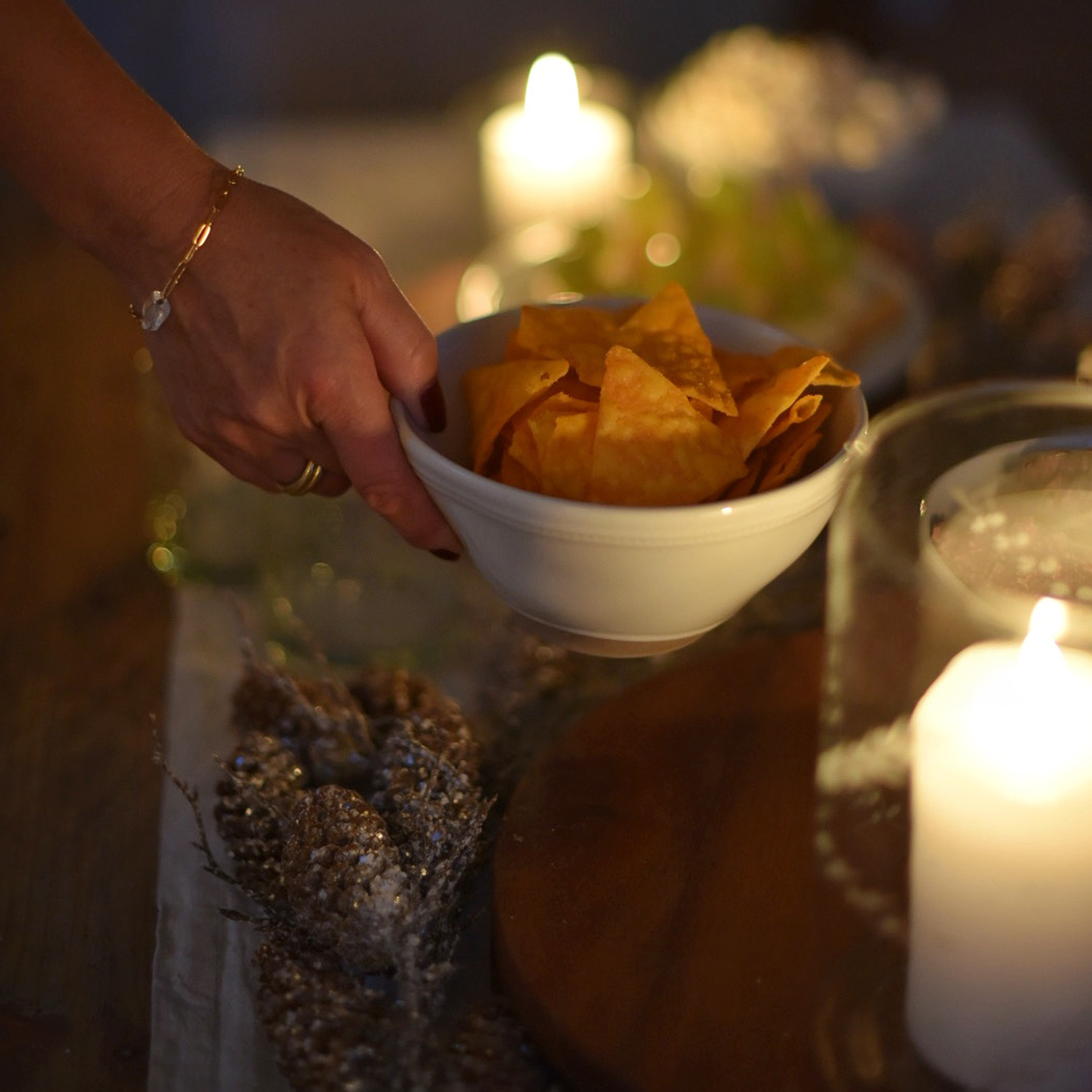 Hand houdt witte kom met oranje chips, op de achtergrond kaarsen en feestelijke decoratie