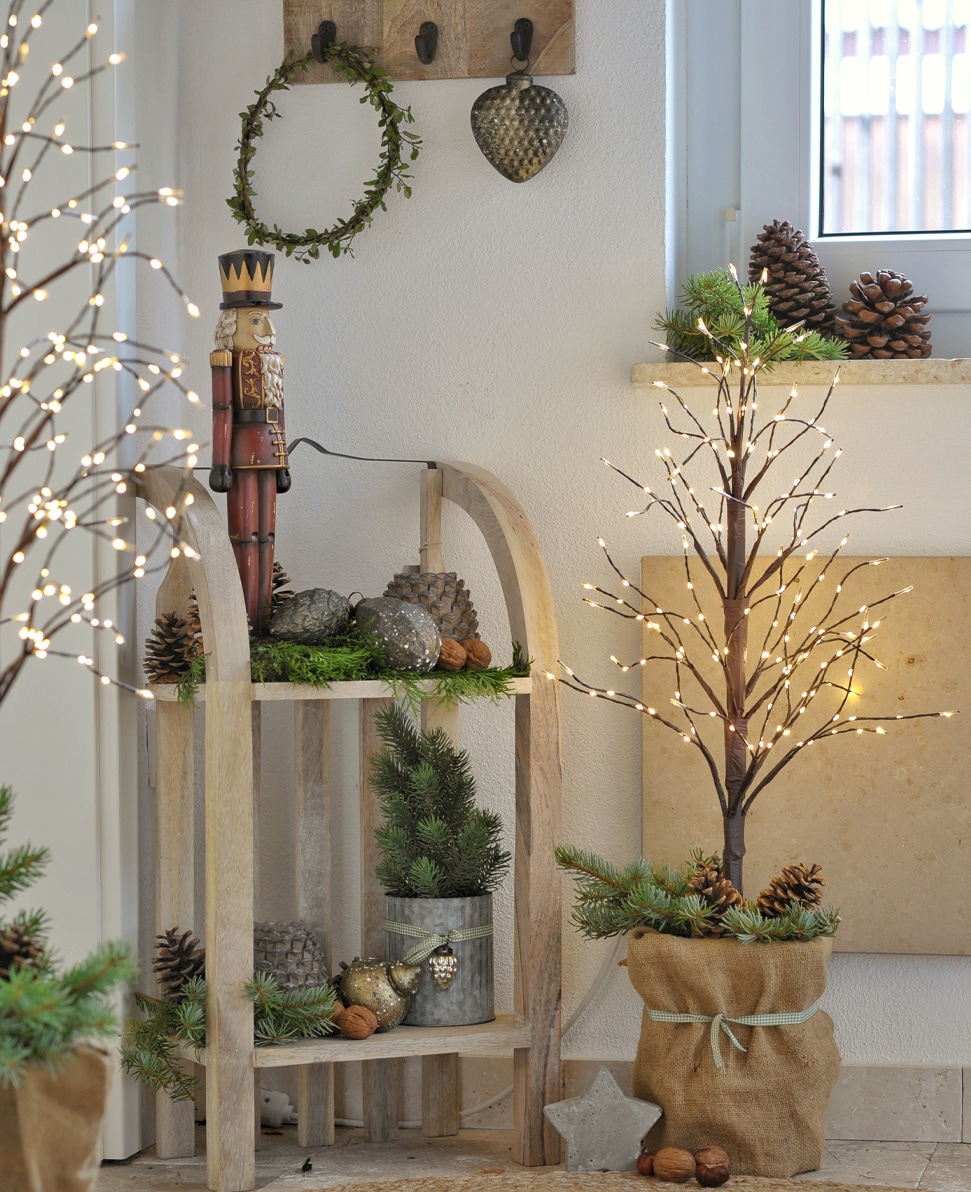 Decoratieve LED-lichtboom in juten zak met dennenappels en groene takken, sfeervolle kerstdecoratie.